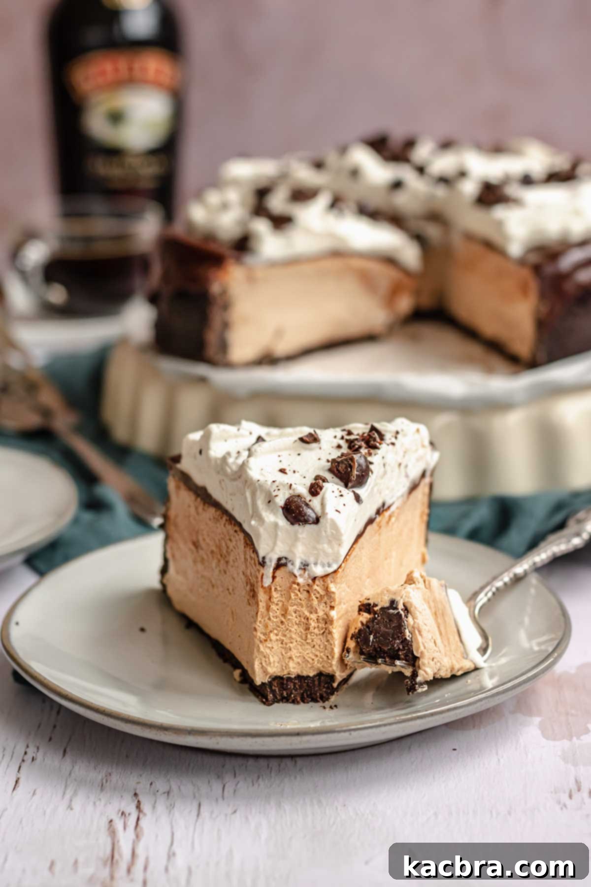 A perfectly sliced no-bake Baileys cheesecake, revealing its creamy layers and rich chocolate ganache, served on a white plate with a fork taking a bite.