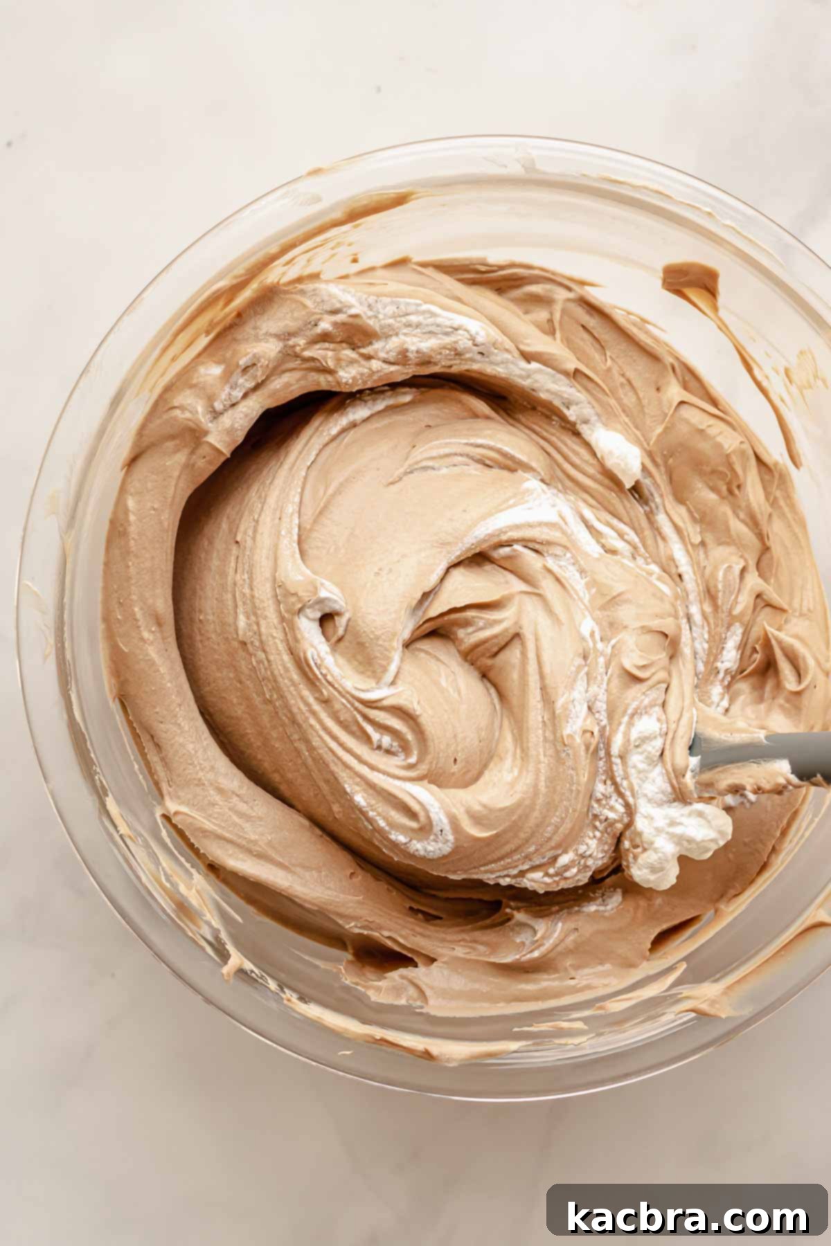 A rubber spatula gently folding stiff whipped cream into the Baileys cheesecake batter, ensuring the airy texture is maintained.