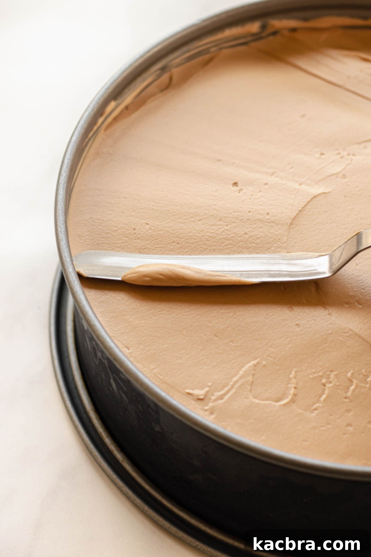 An offset spatula expertly smoothing the Baileys cheesecake batter into an even layer within the springform pan, creating a perfectly flat top.