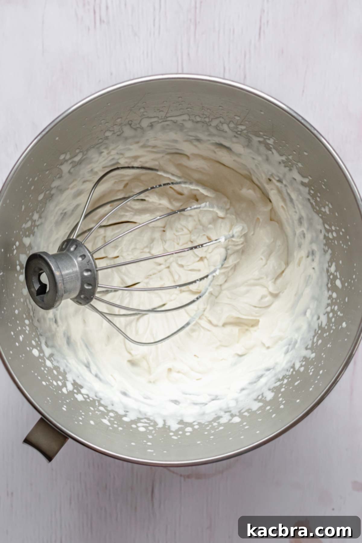 Fluffy Baileys whipped cream in a mixing bowl with a whisk, showing its stiff peaks and light texture, ready for topping the cheesecake.