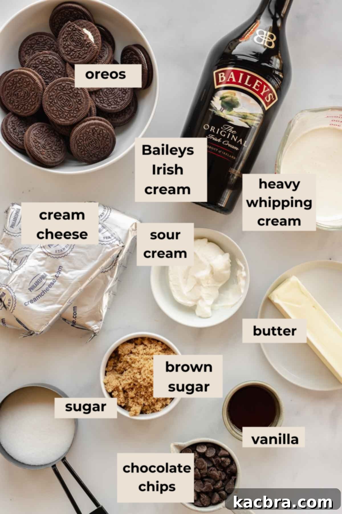 A flat lay photograph showcasing all the fresh ingredients for a homemade Baileys no-bake cheesecake, including Oreos, cream cheese, Baileys Irish Cream, chocolate chips, and heavy whipping cream.