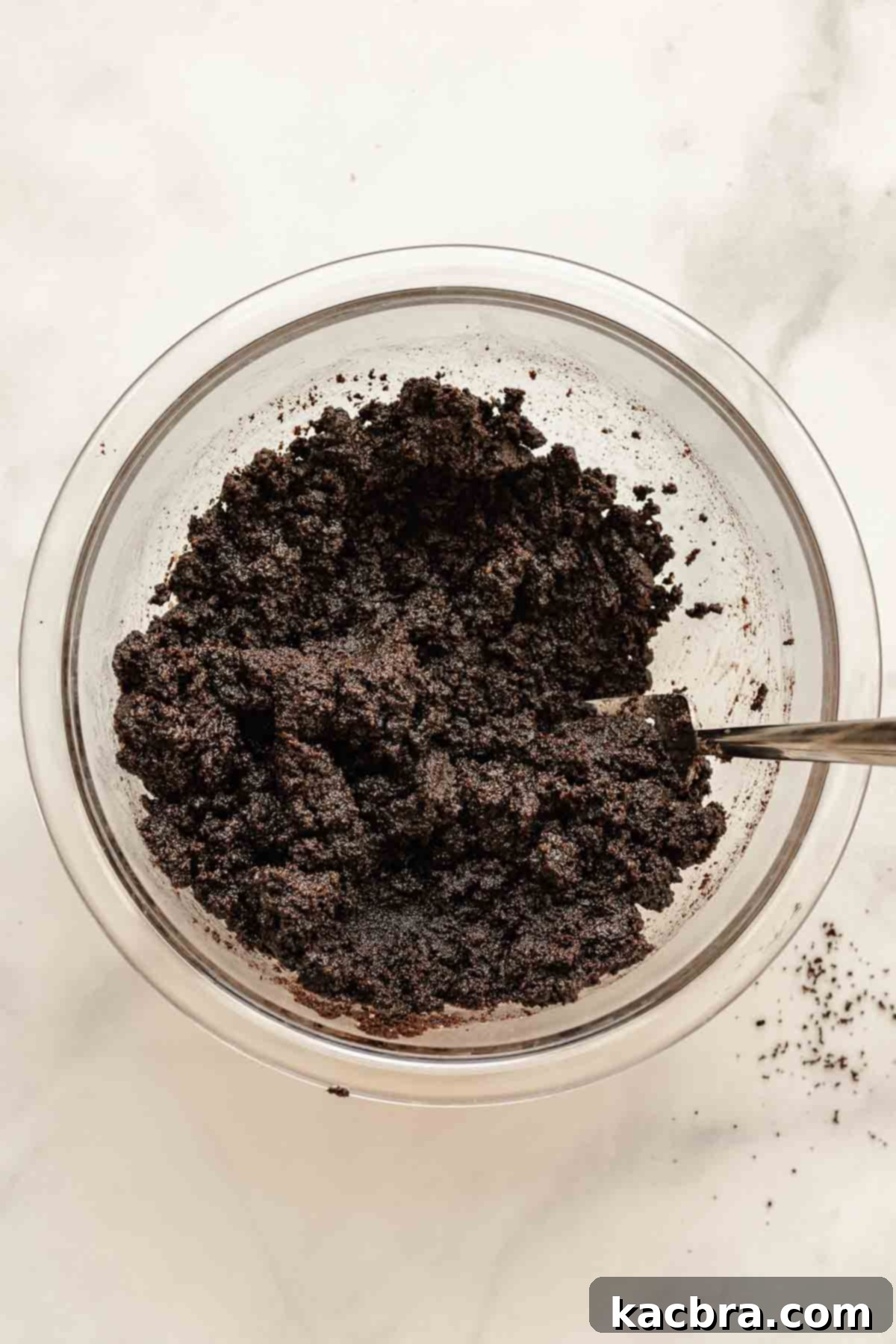 A bowl of crushed Oreo crumbs mixed with melted butter, brown sugar, and salt, ready to form the base of the cheesecake.