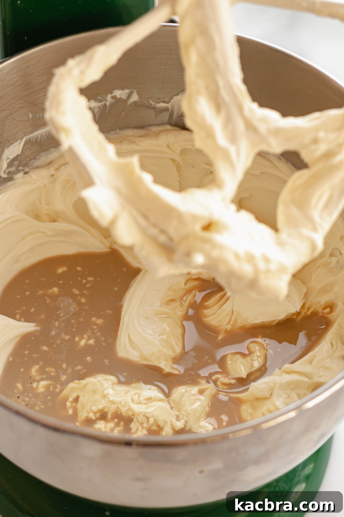 A stream of Baileys Irish Cream being poured into the fluffy cream cheese mixture in a stand mixer bowl, with a splash of vanilla extract also visible.