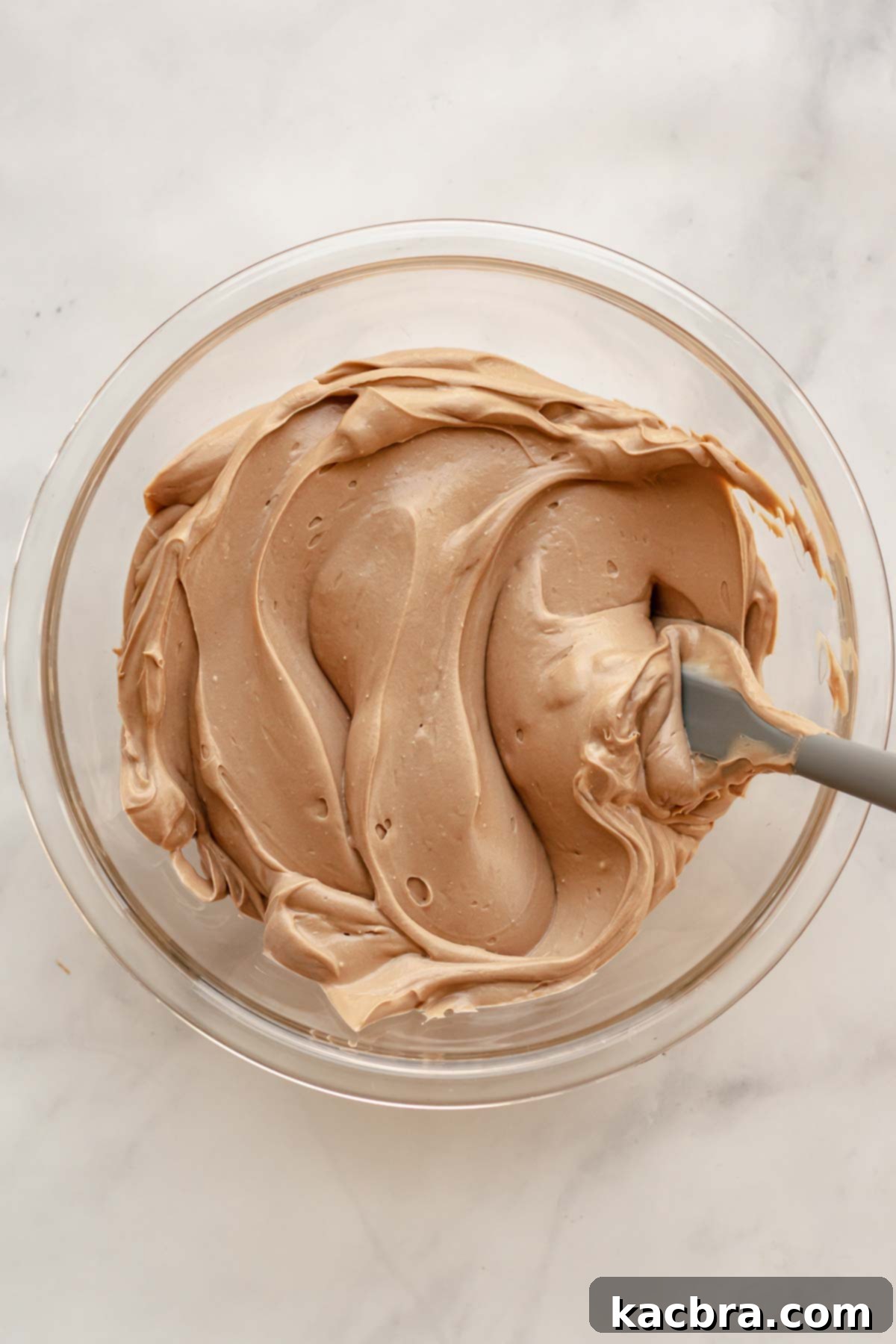 Melted semi-sweet chocolate being mixed into the Baileys cheesecake batter in a bowl, creating a rich chocolatey hue and smooth consistency.