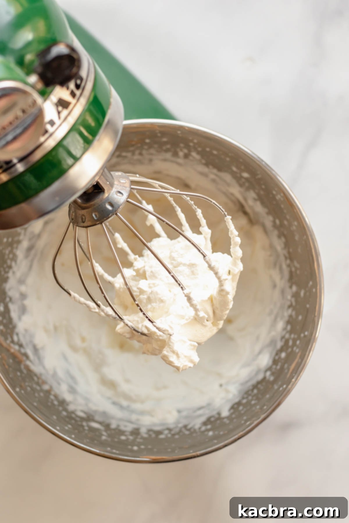 Stiff peaks of freshly whipped heavy cream visible on the whisk attachment of a stand mixer, indicating perfectly whipped cream.