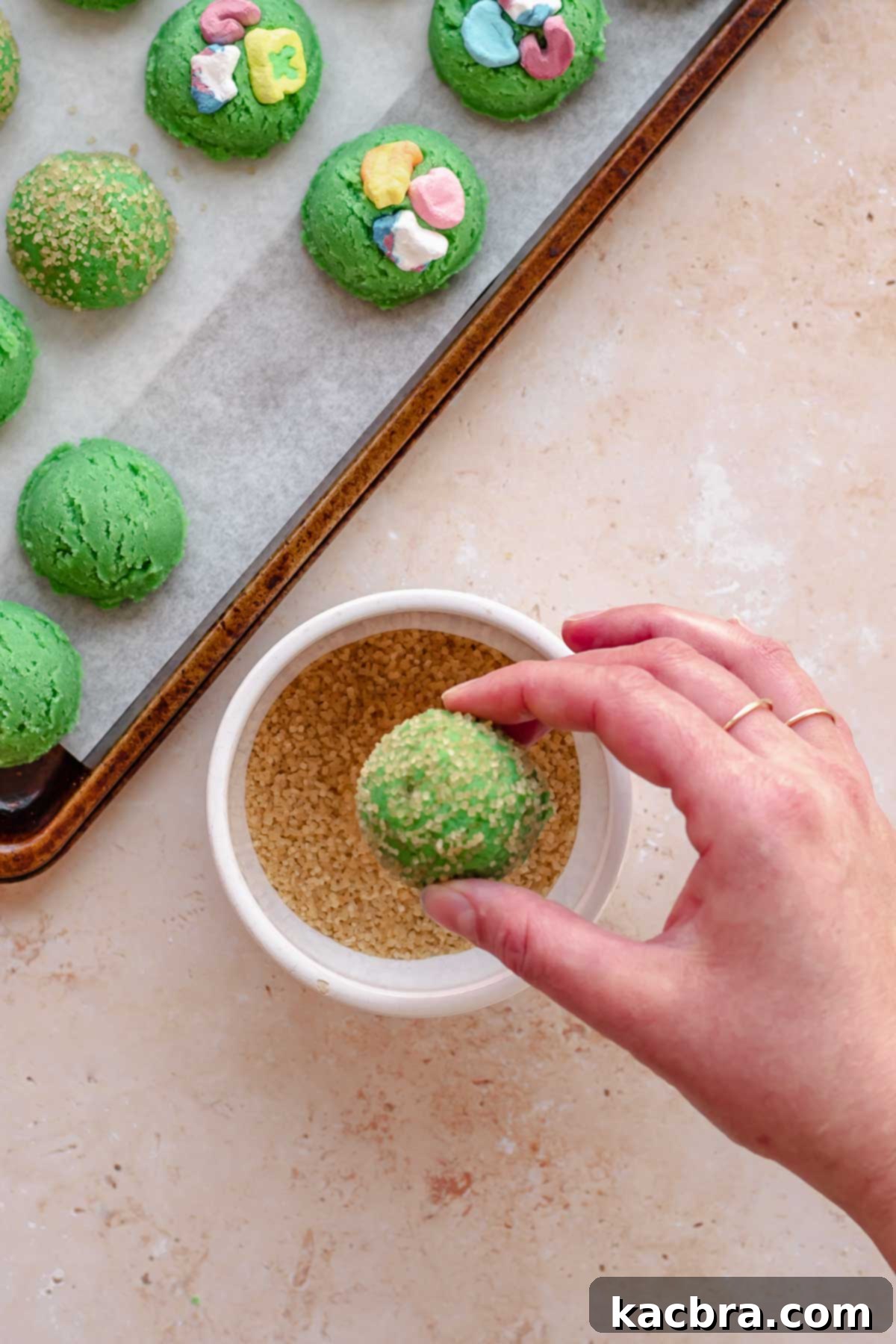 A hand rolls a cookie dough ball through coarse sugar.