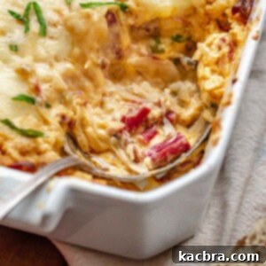 A spoon rests in a casserole dish with dip on it.