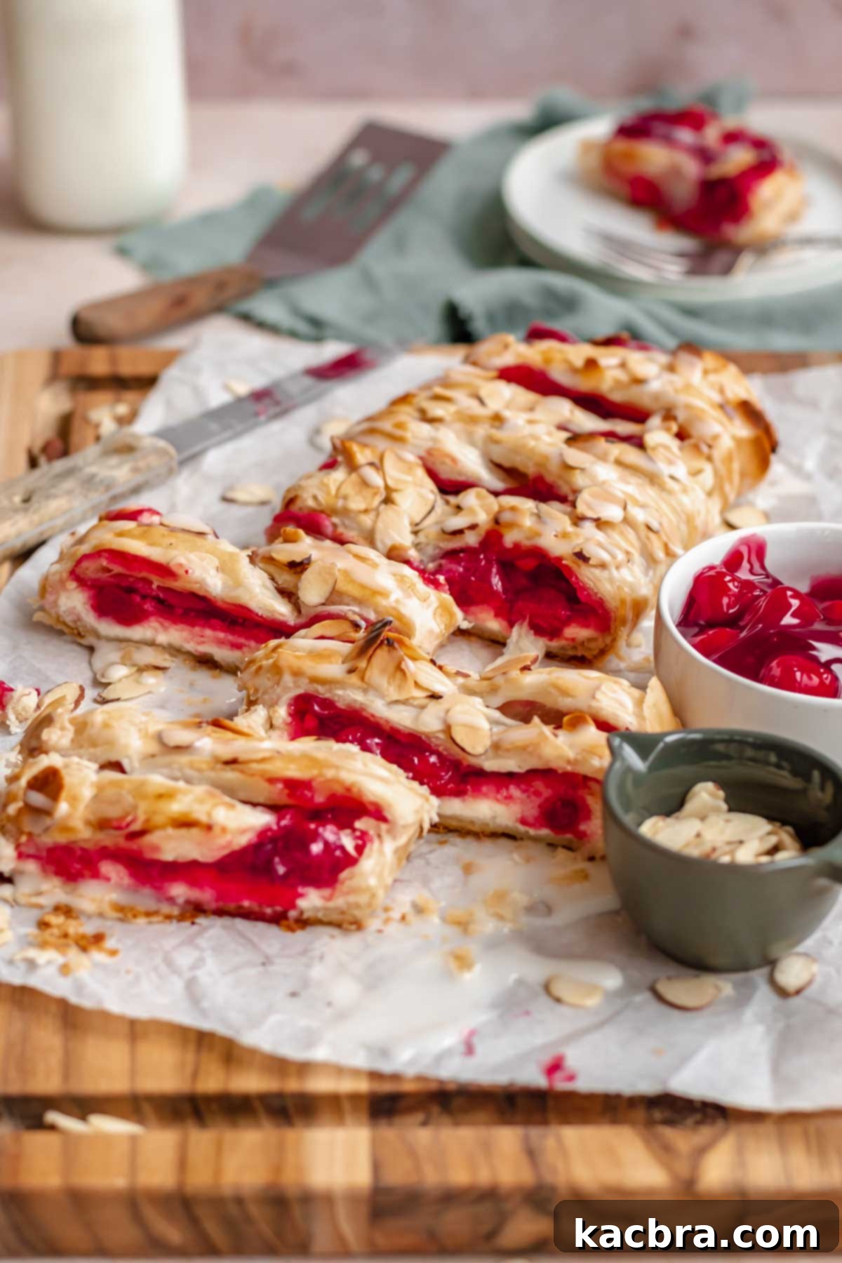 A freshly baked cherry danish on a cutting board, drizzled with almond glaze and sliced.