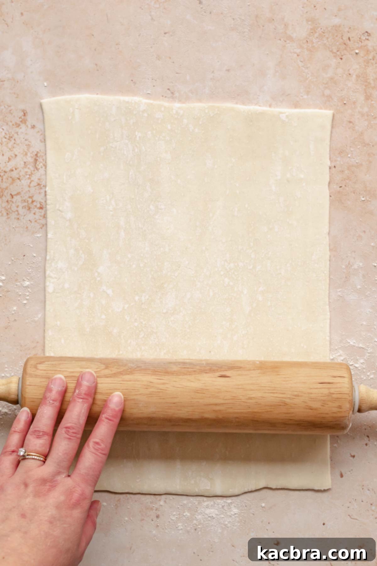 Flaky Cherry Cream Cheese Pastry 4 A rolling pin gently rolls out puff pastry into a uniform rectangle on a parchment-lined baking sheet.