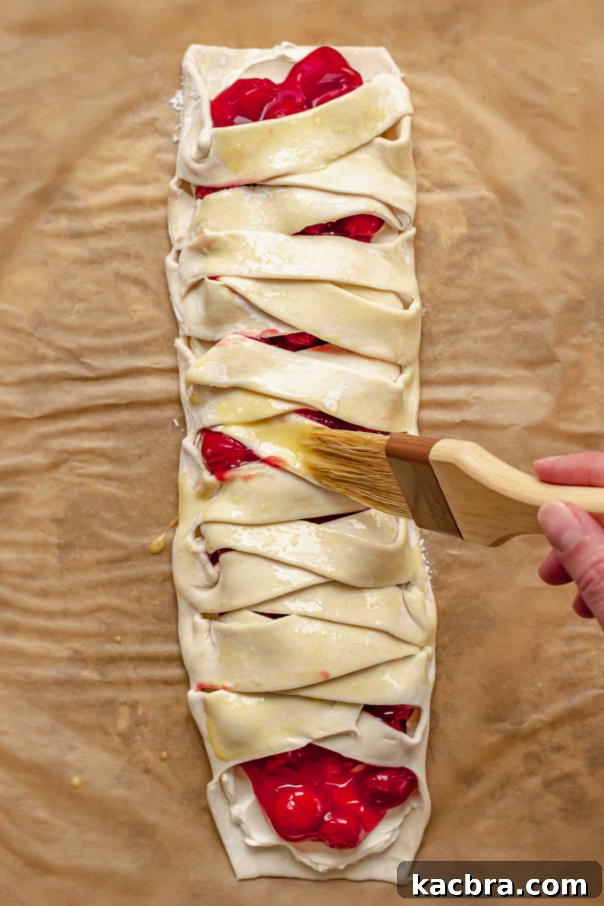 A brush applies egg wash on top of the assembled danish, ready for baking.