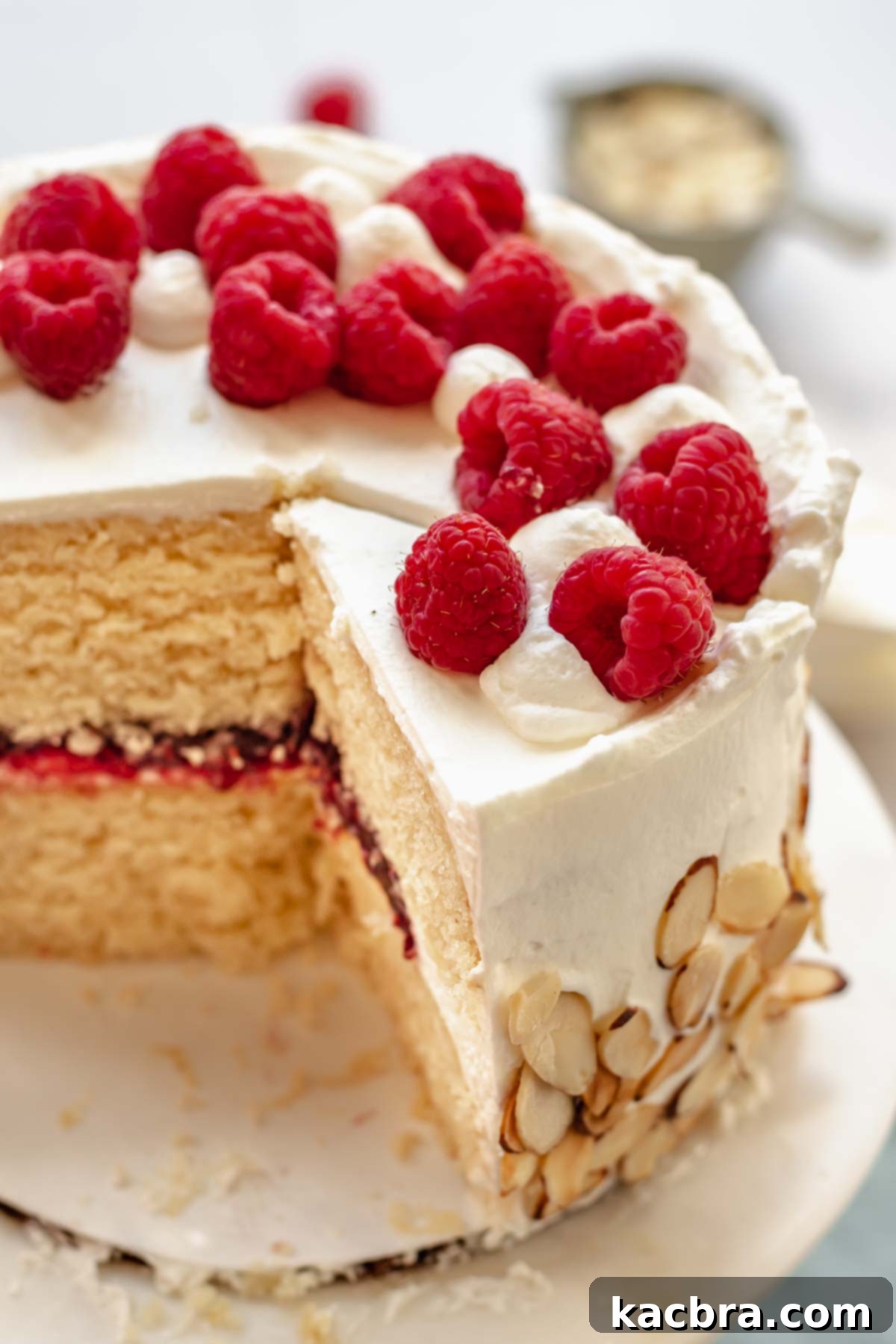 Crimson Kissed Almond Delight 2 A beautifully frosted raspberry almond cake on a platter, with several slices already served, showcasing the layers of cake and jam.
