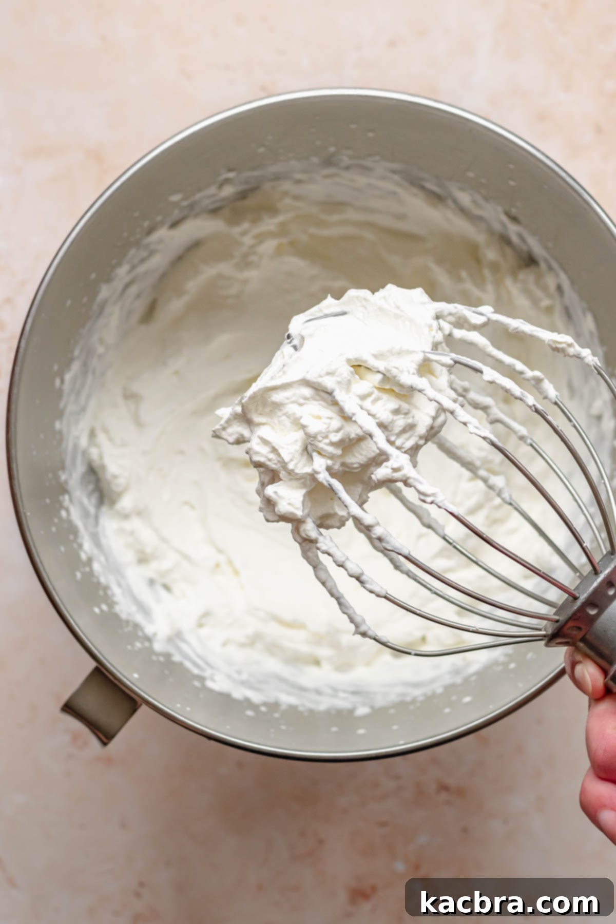 Crimson Kissed Almond Delight 11 A whisk attachment covered in perfectly whipped heavy cream, holding stiff peaks.