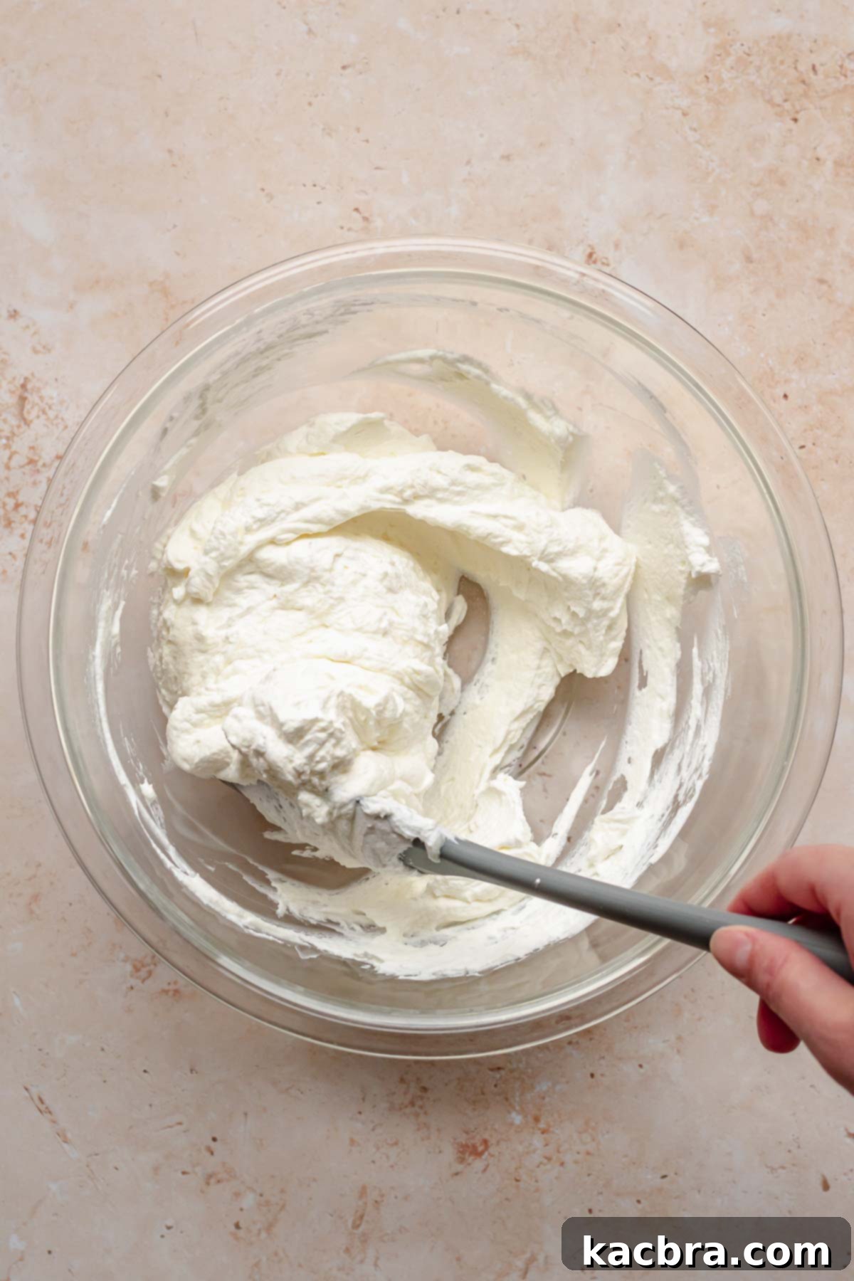 Crimson Kissed Almond Delight 12 A spatula gently folding whipped cream into the cream cheese mixture until light and fluffy.