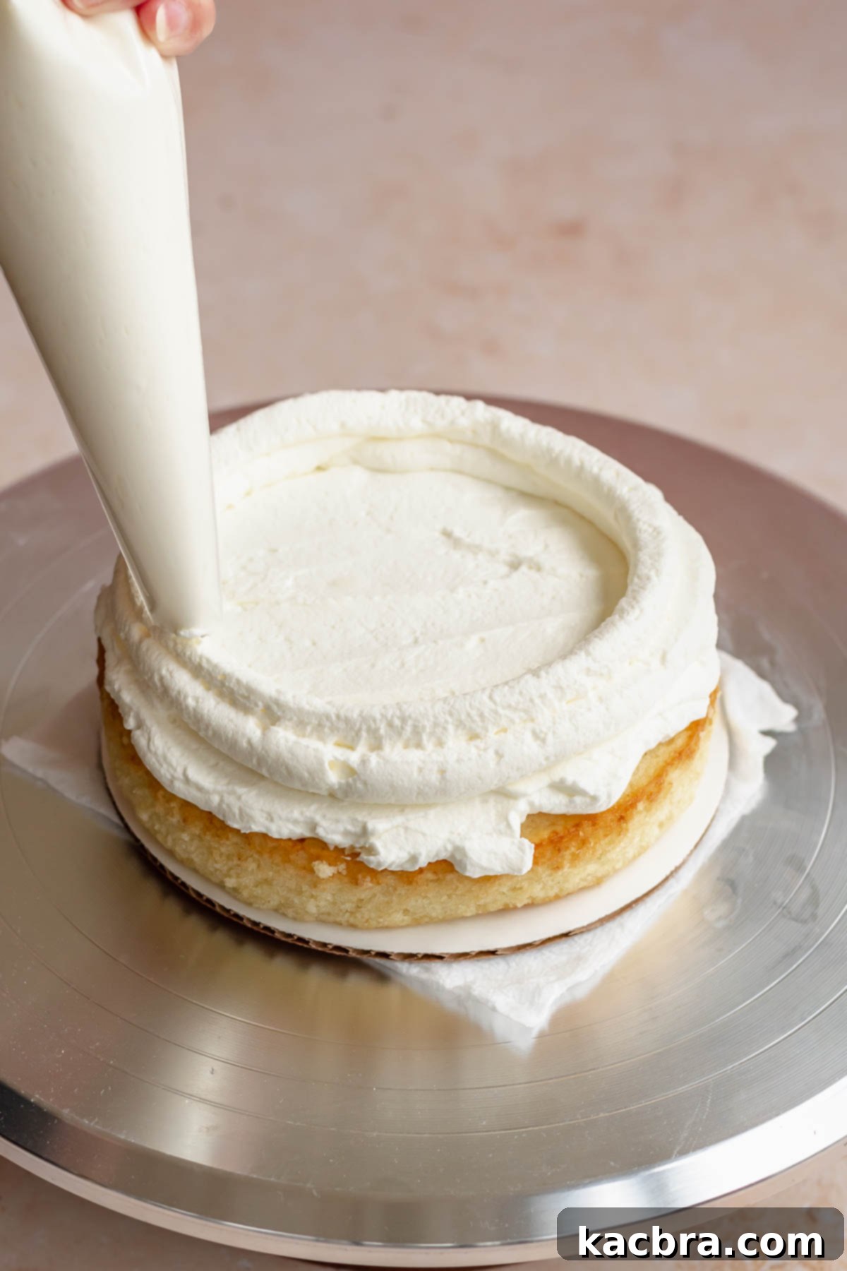 Crimson Kissed Almond Delight 13 A piping bag creating a frosting dam around the edge of the bottom cake layer.