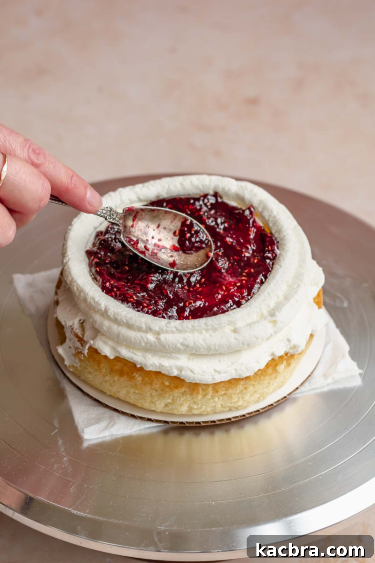 Crimson Kissed Almond Delight 14 Raspberry jam being smoothed into the center of the cake layer, inside the frosting dam.
