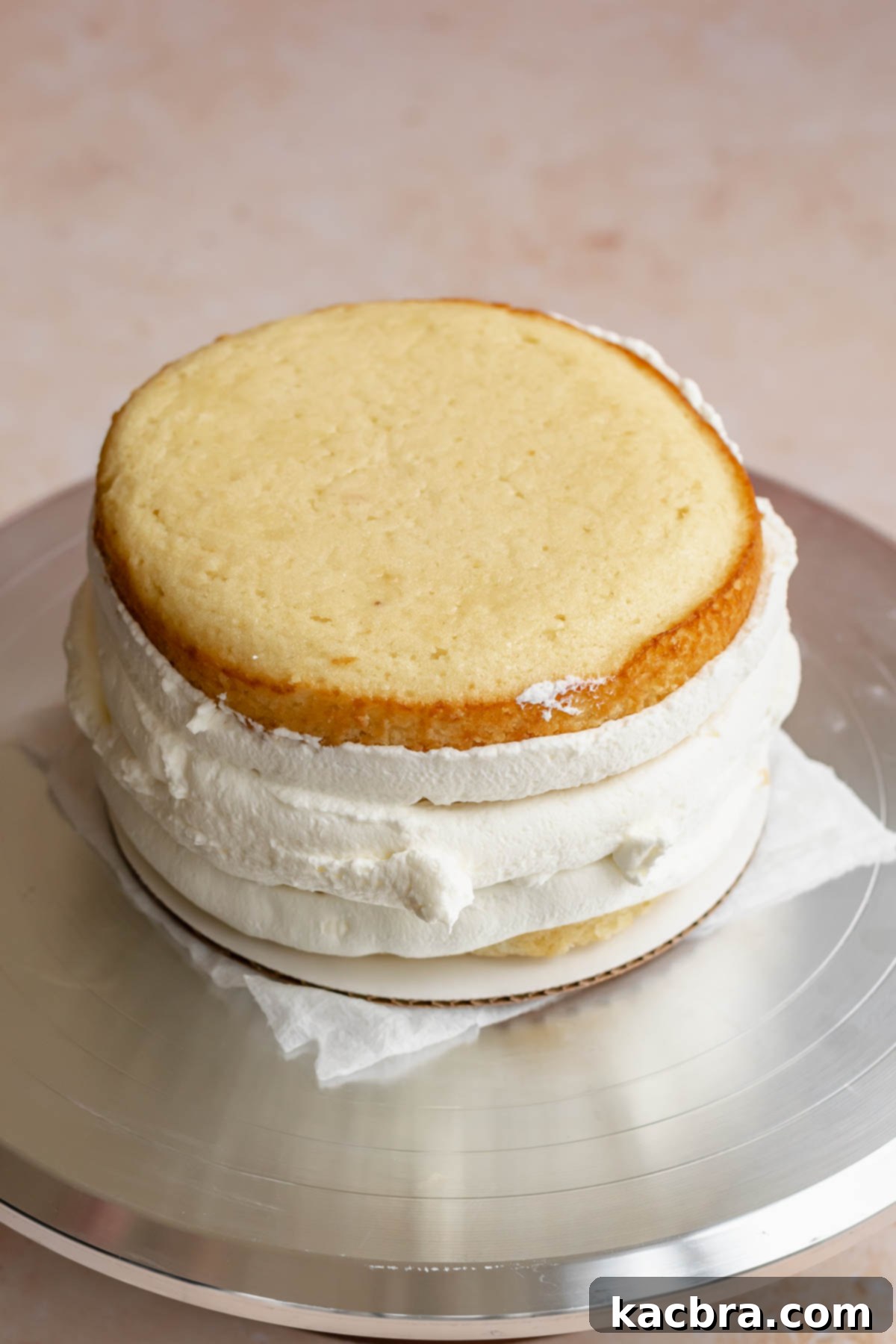 Crimson Kissed Almond Delight 15 The second cake layer placed on top of the jam, with frosting beginning to cover the sides.