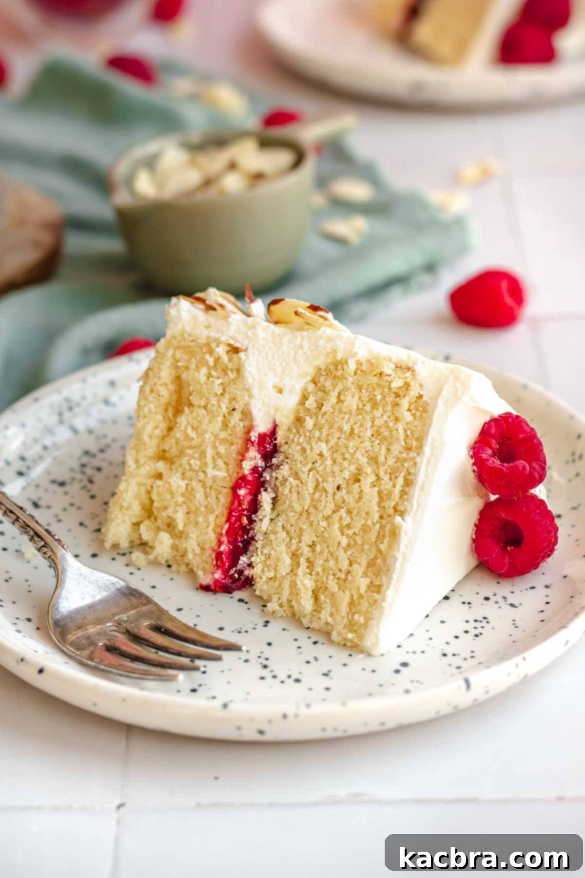 Crimson Kissed Almond Delight 19 A beautiful slice of raspberry almond cake with frosting and raspberries on a white plate.