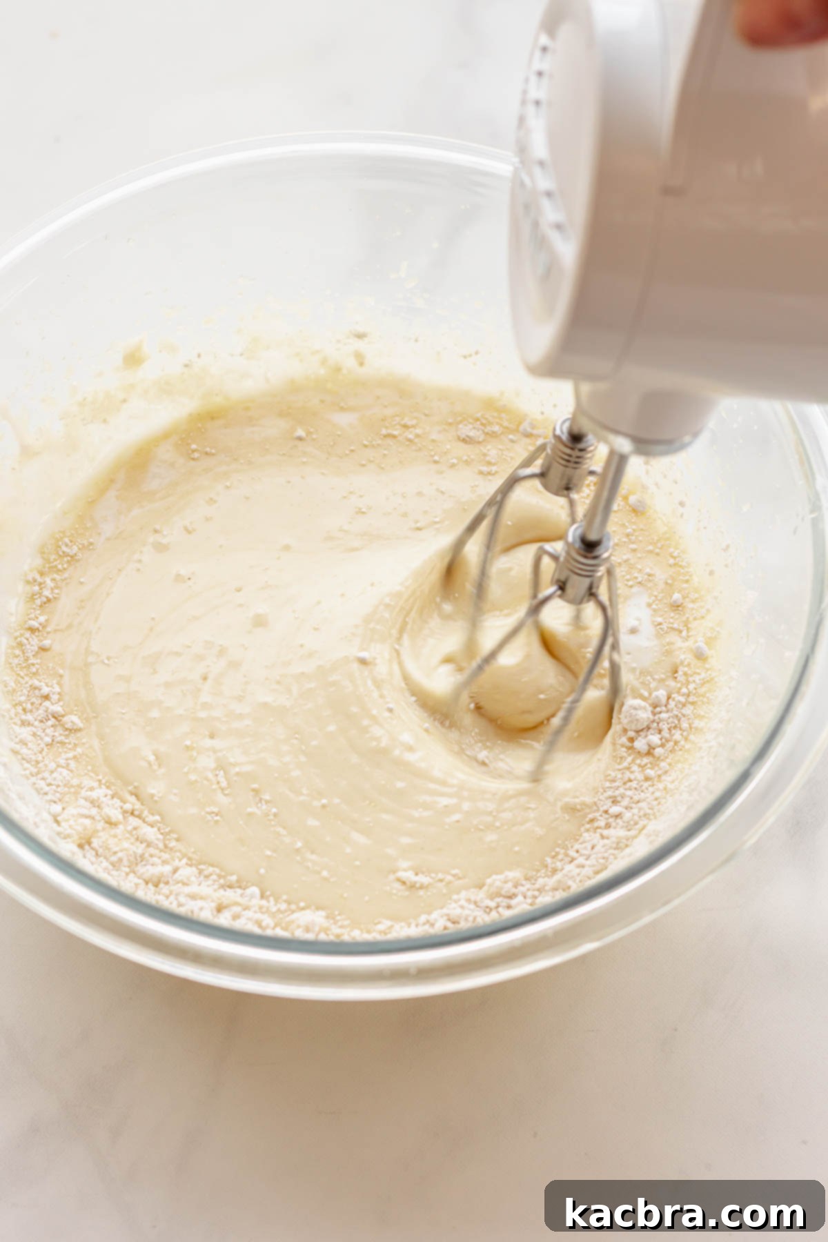 Crimson Kissed Almond Delight 8 A hand mixer blending flour into cake batter, alternating with buttermilk.