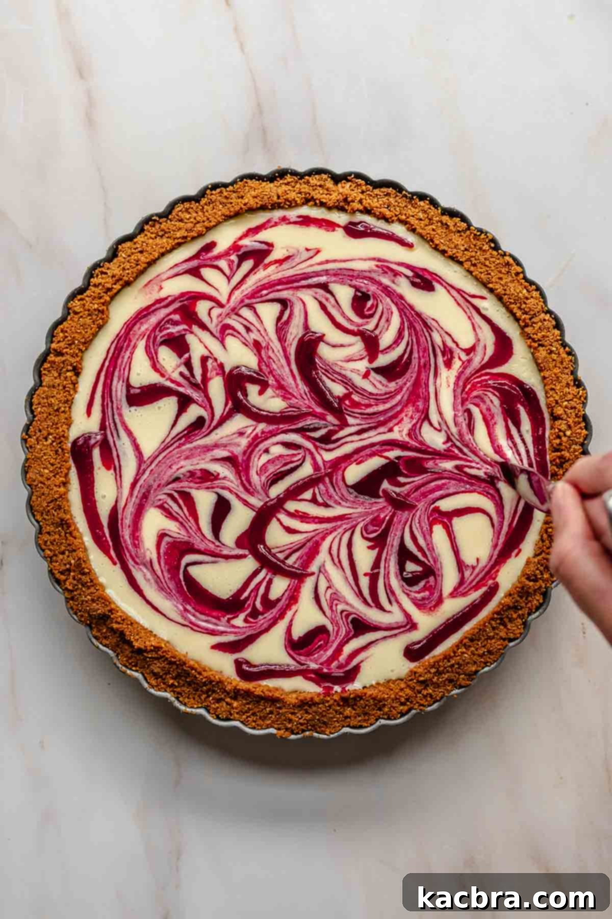 A butter knife being used to swirl the cranberry puree and white chocolate ganache together into an artistic pattern.