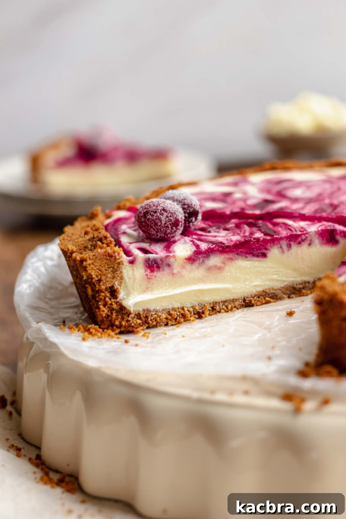 A cross-section view of the white chocolate cranberry tart, showcasing the distinct layers of crust, ganache, and cranberry swirl, topped with sugared cranberries.