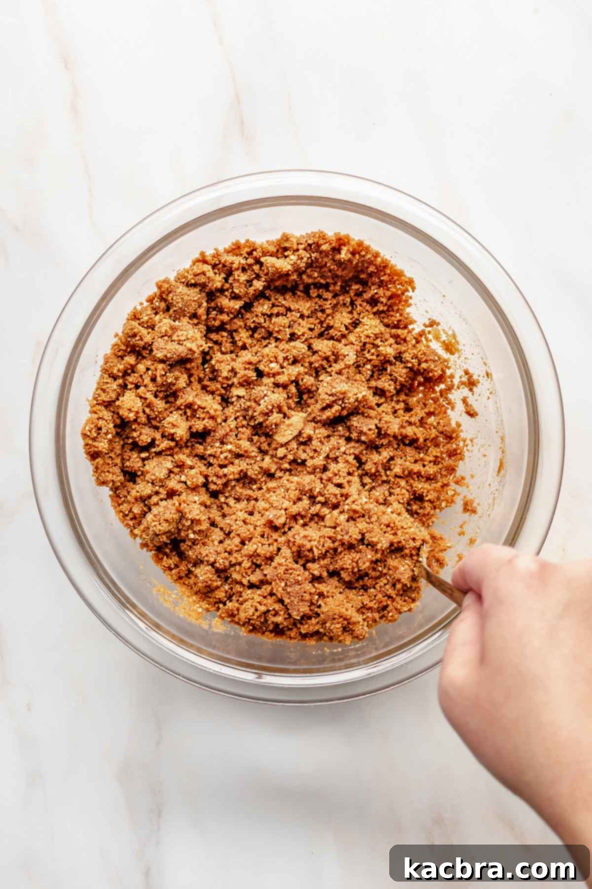 A hand mixing Biscoff cookie crumbs with melted butter and salt in a bowl, preparing the tart crust.