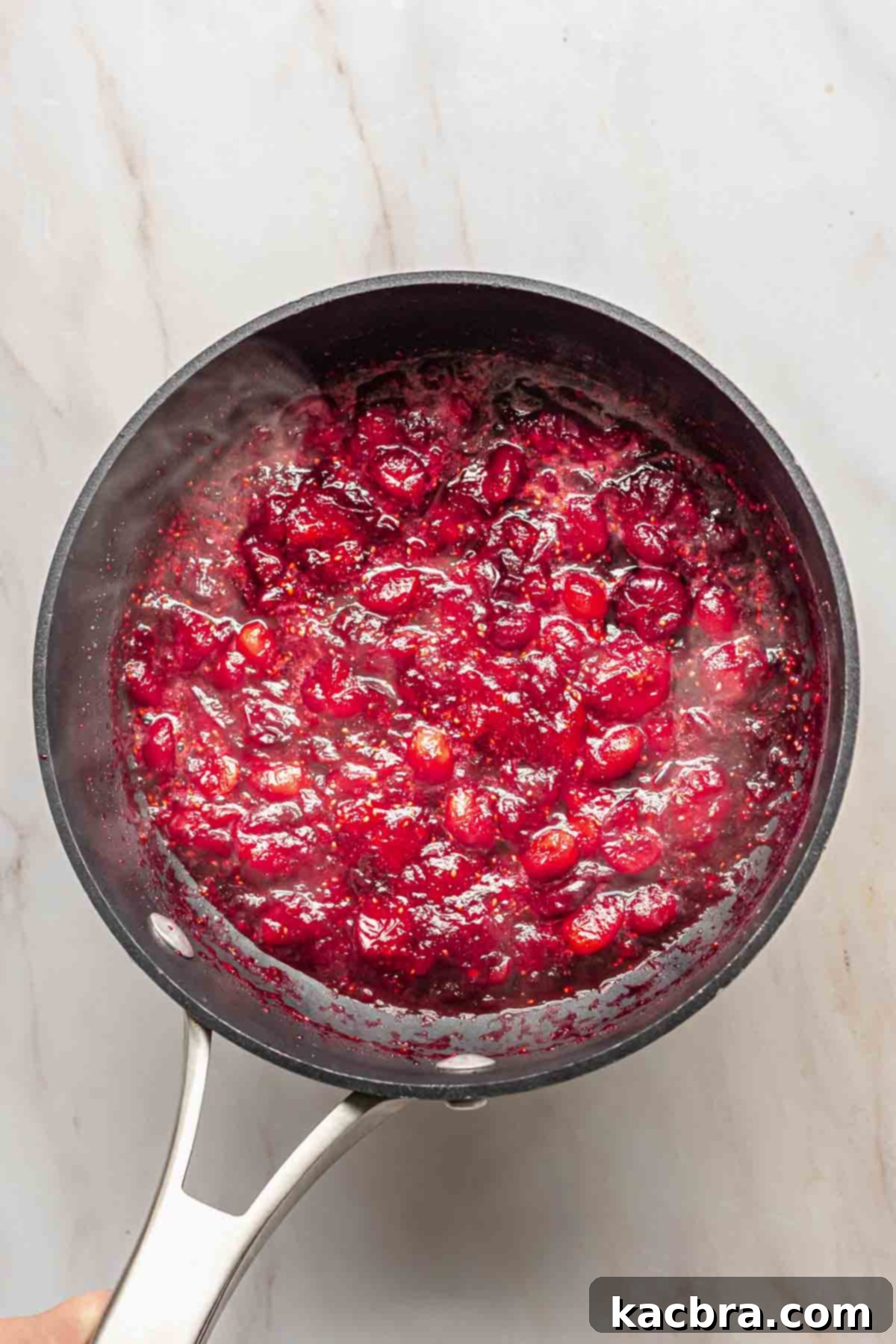 Fresh cranberries cooking down with sugar and water in a saucepan over medium heat.