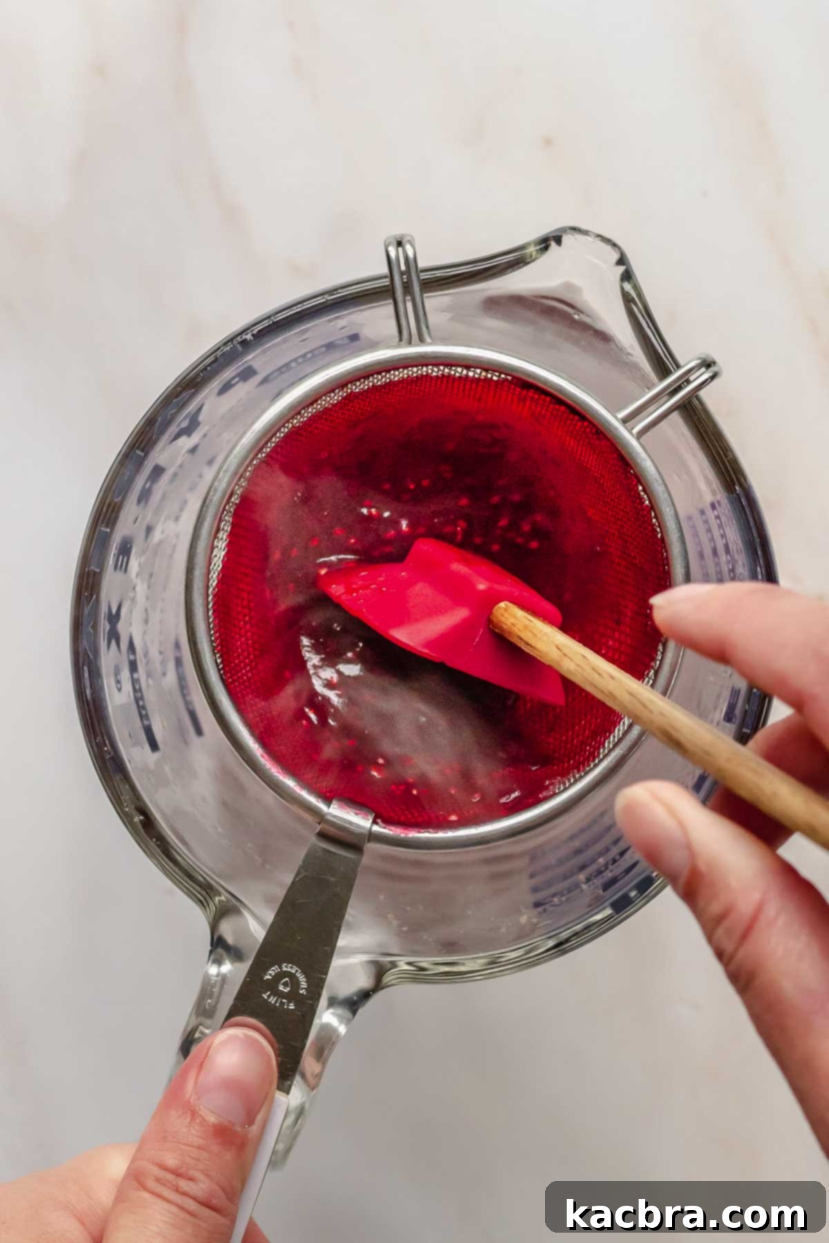 A hand pressing cooked cranberry puree through a fine mesh sieve into a bowl, ensuring a smooth consistency.