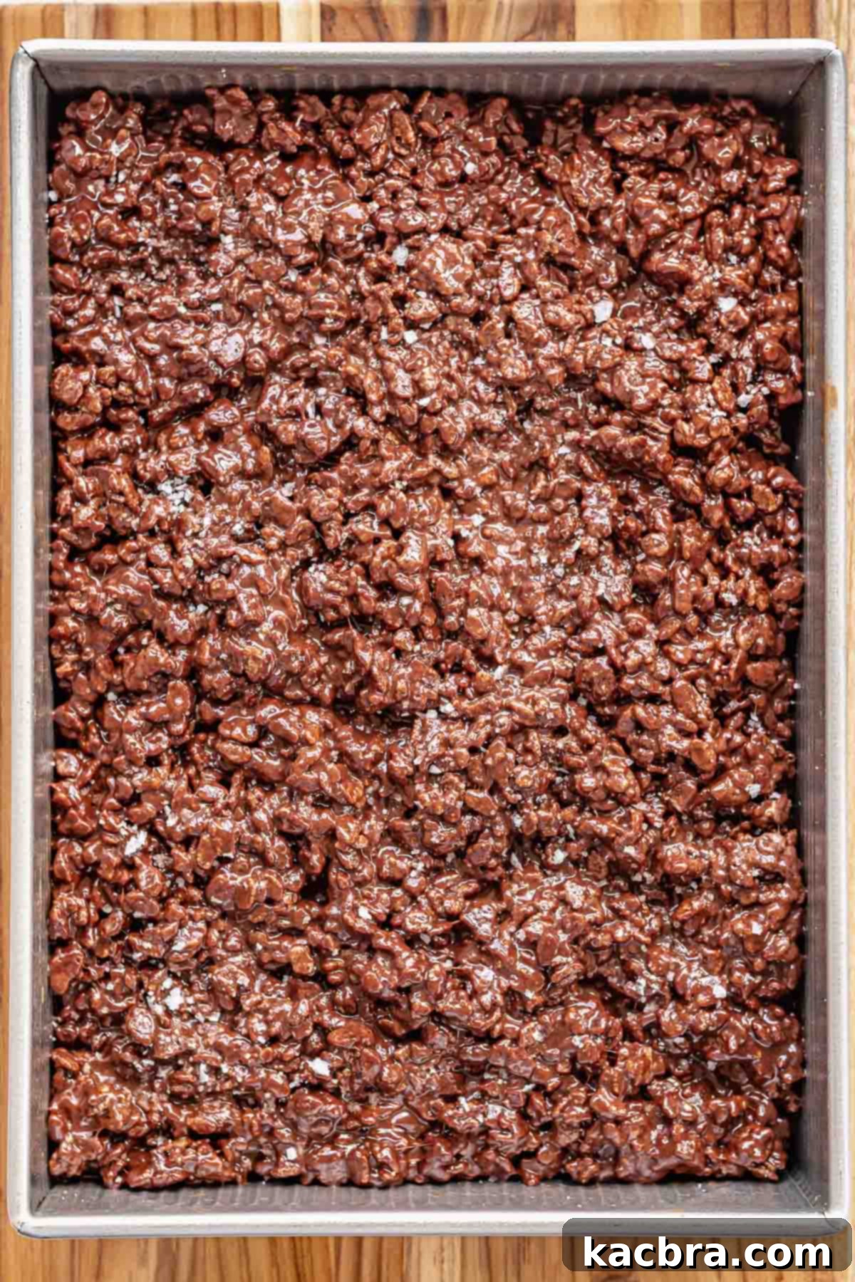 Chocolate Rice Krispie treats in a pan, generously sprinkled with flaky sea salt on top.