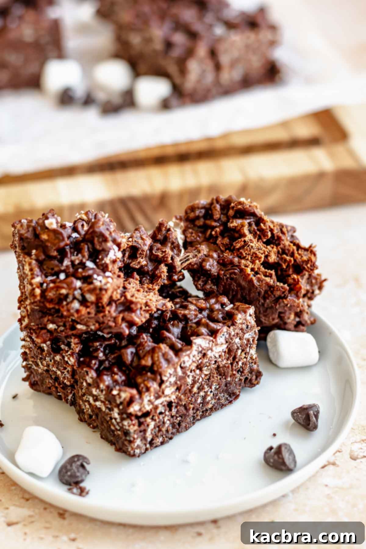 Chocolate Rice Krispies on a plate. One square is pulled apart to show its chewy interior.