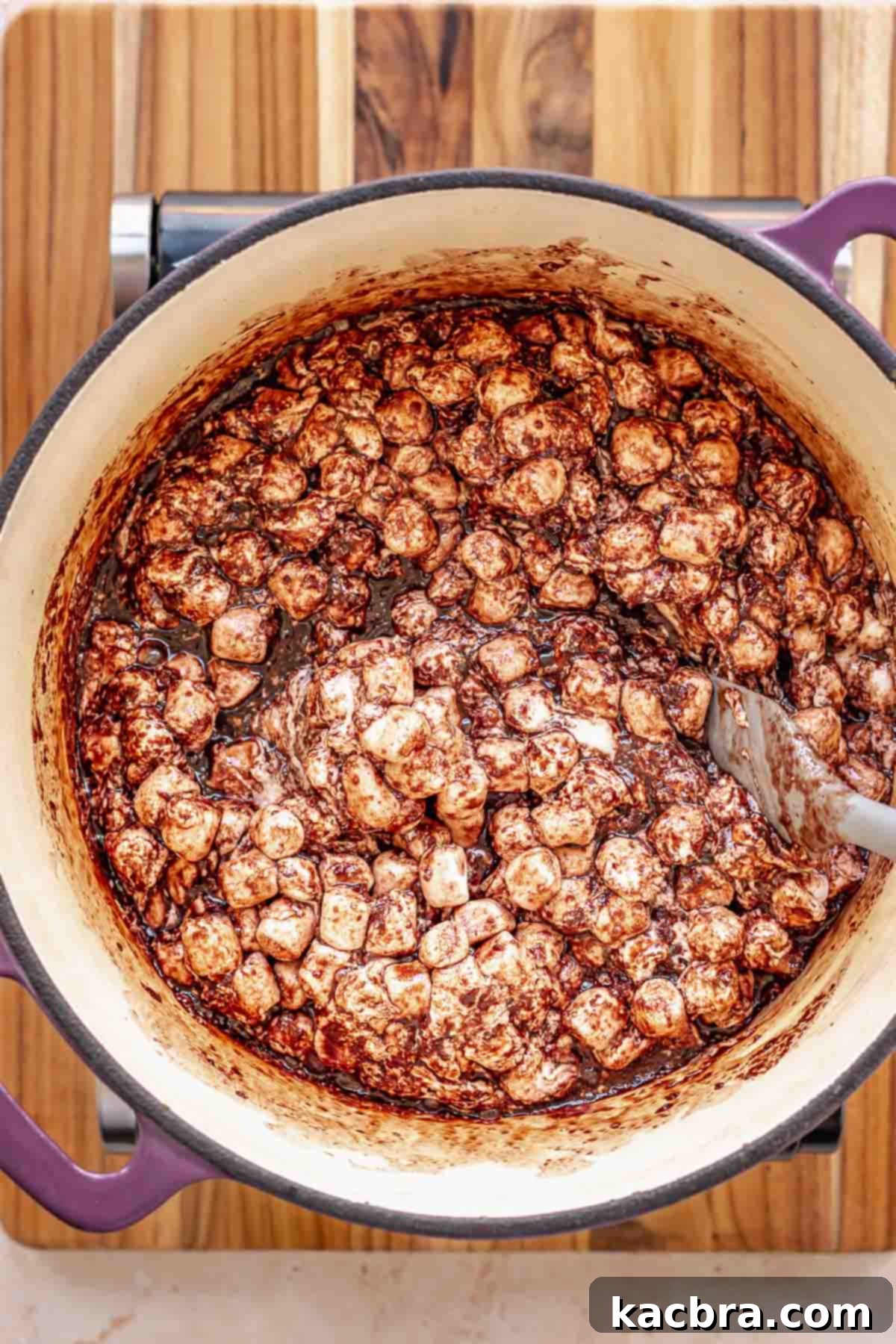 A spatula stirring mini marshmallows into the chocolate mixture in a pot.