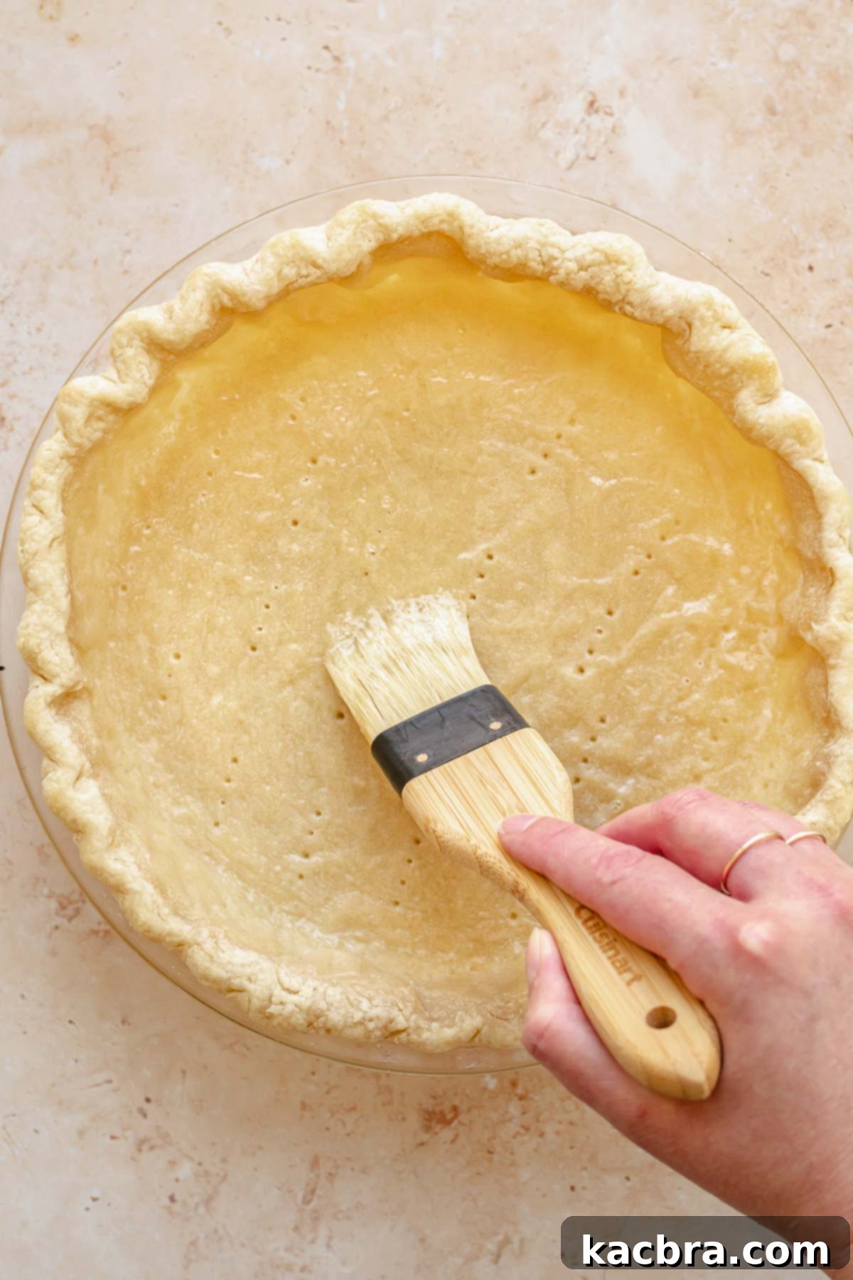 A pastry brush applies egg whites to a par-baked pie crust to seal it.
