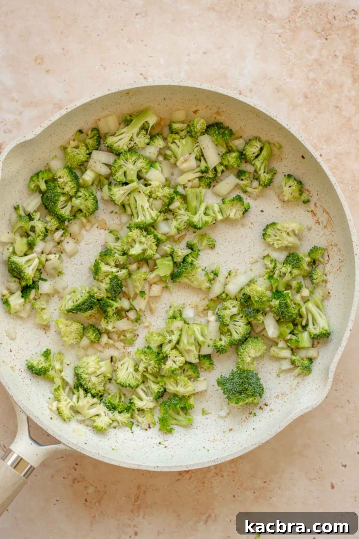 Broccoli florets, diced onion, and minced garlic sautéing in bacon fat in a pan.