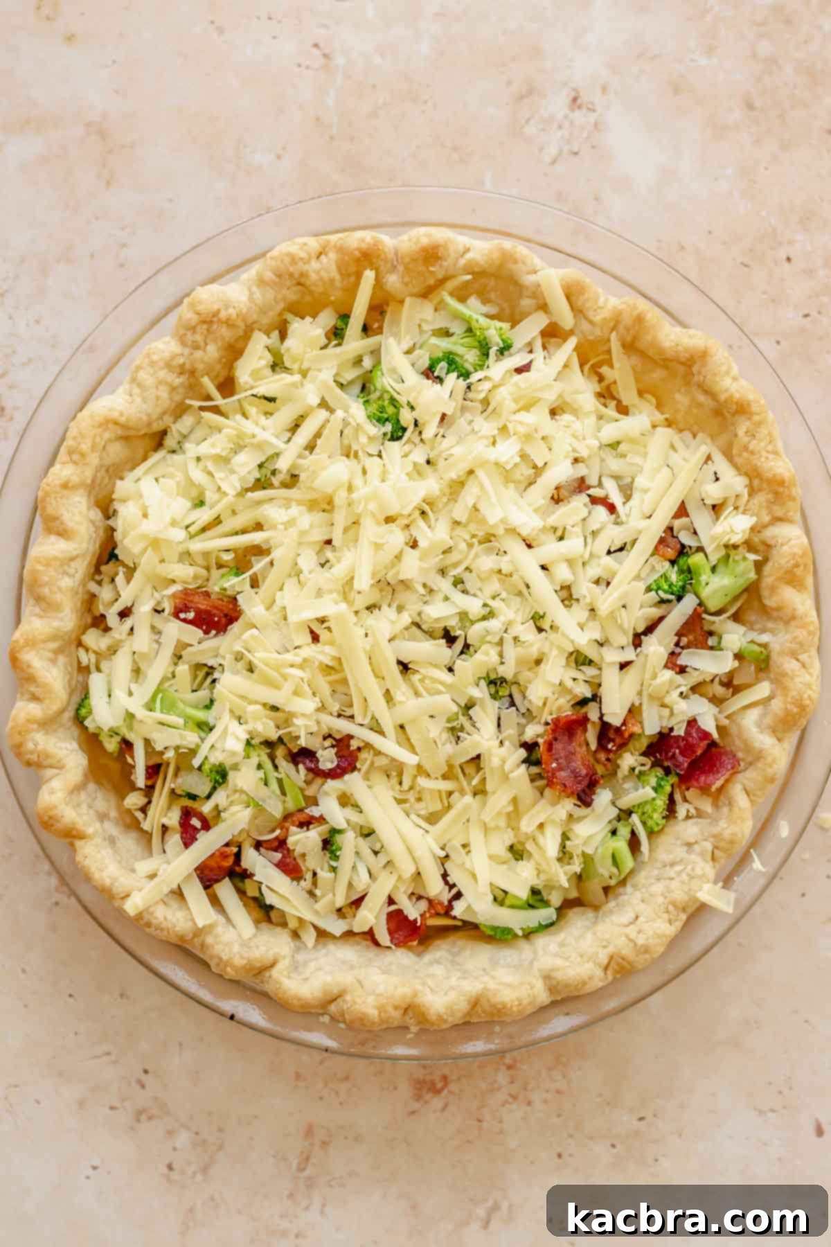 Cooked bacon, broccoli, onion, garlic, and shredded cheese spread evenly in a par-baked pie crust.