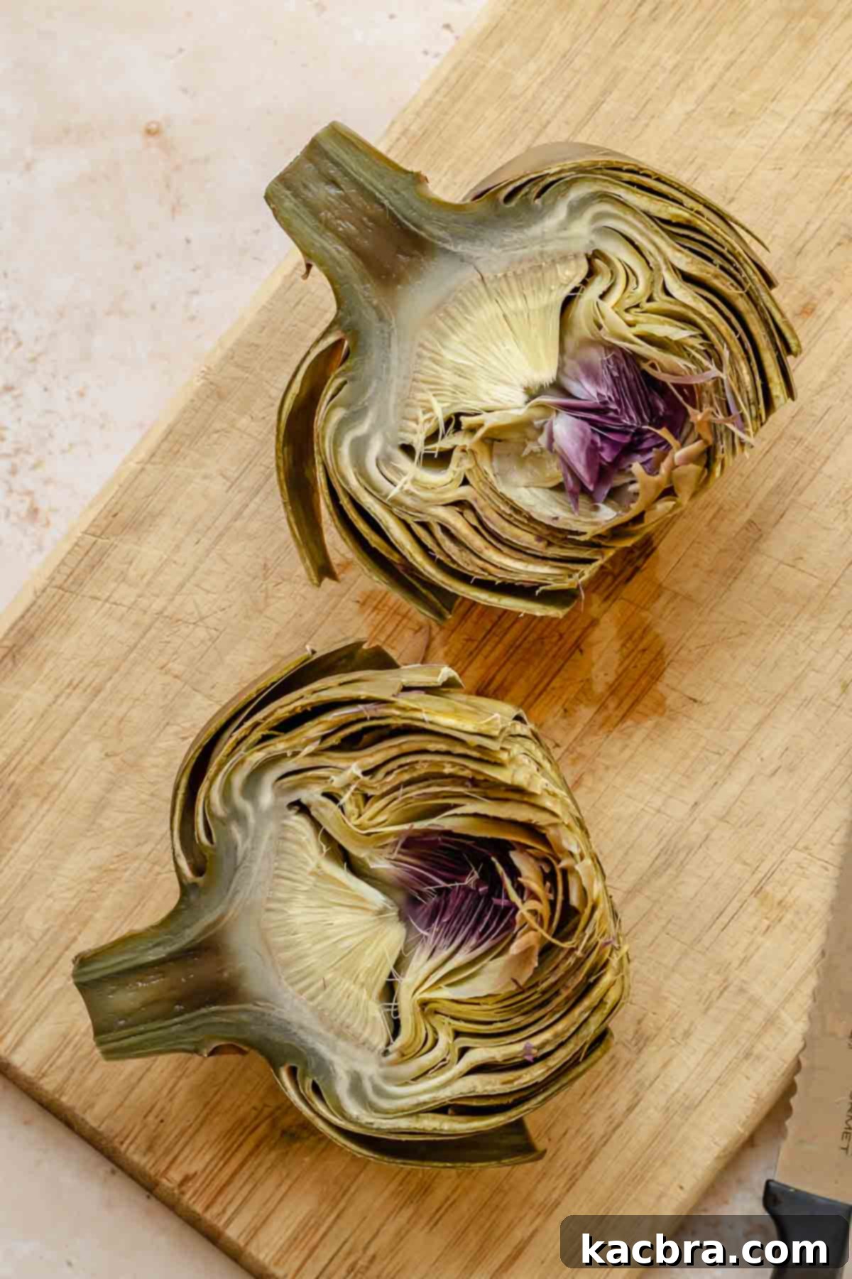 Steamed artichokes cut in half on a cutting board.