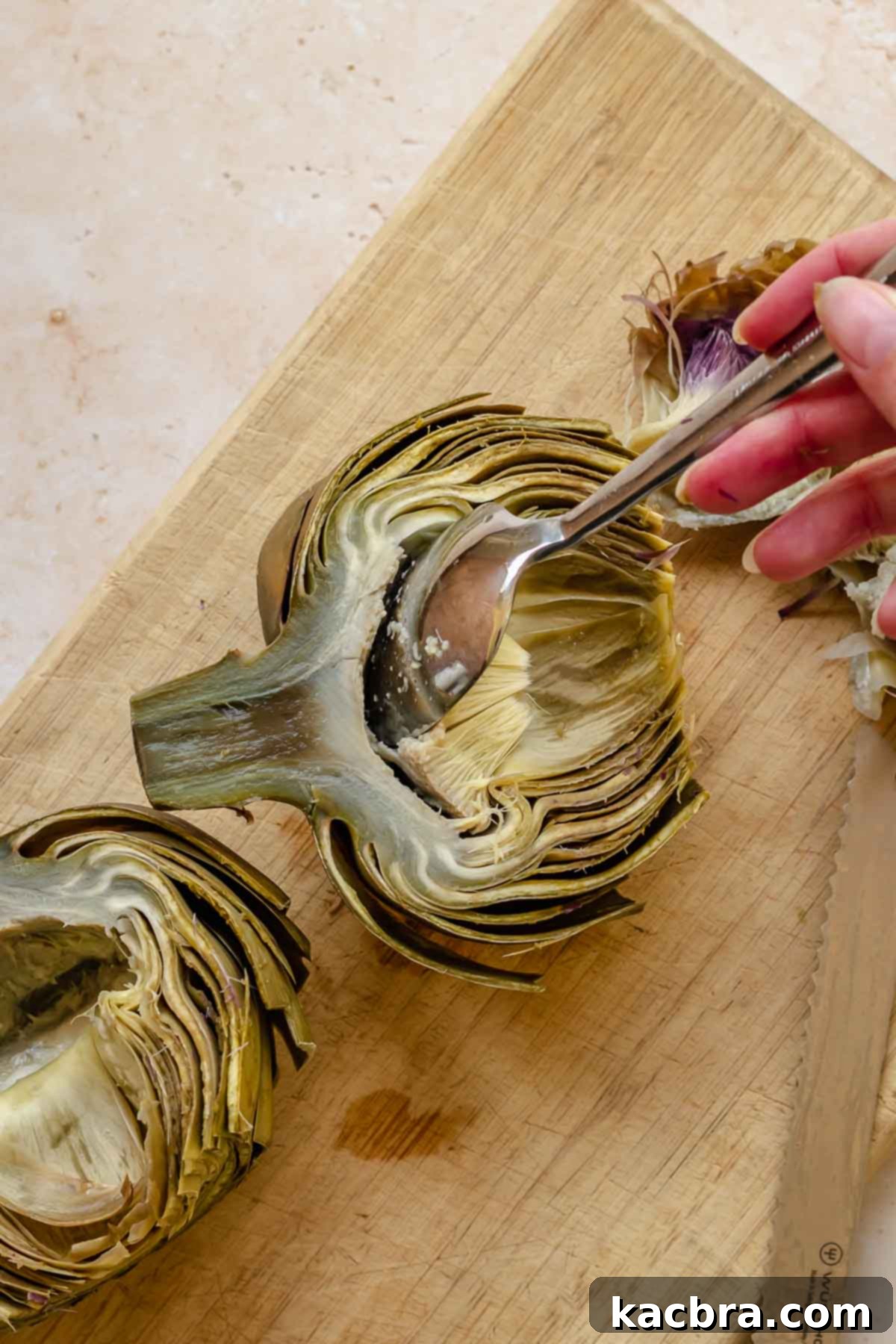 A spoon removes the choke from half of a steamed artichoke.