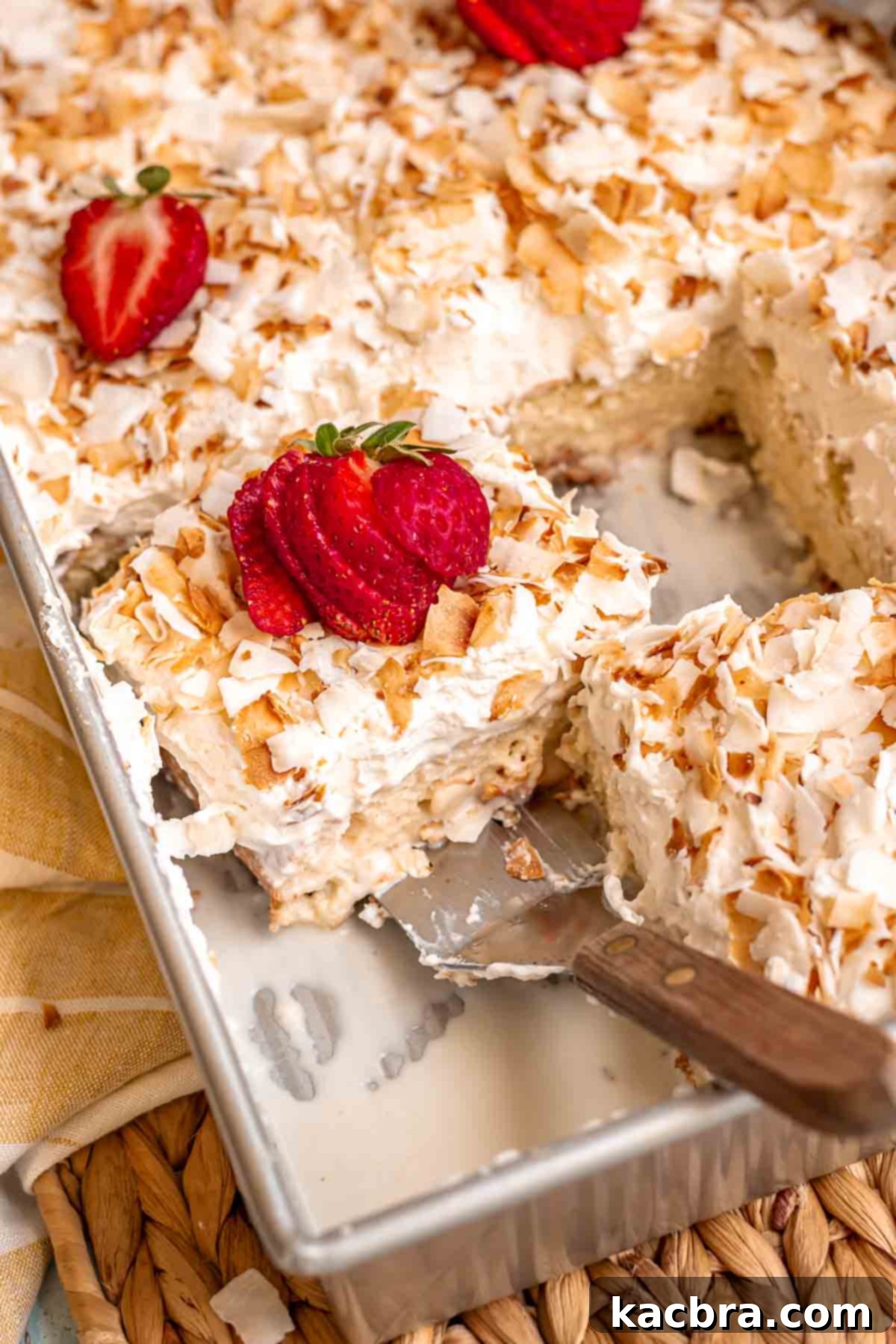 A spatula removes a soaked piece of coconut tres leches cake from a pan, showing its moist texture.