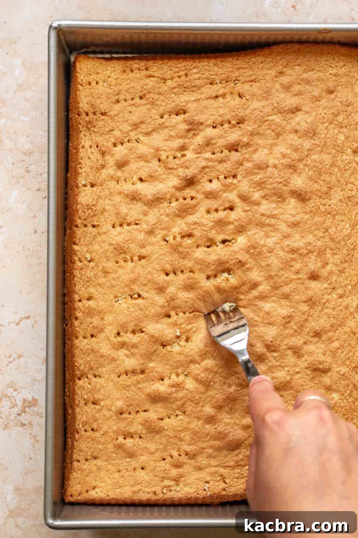 A fork creates numerous pricks across the surface of the baked sponge cake.