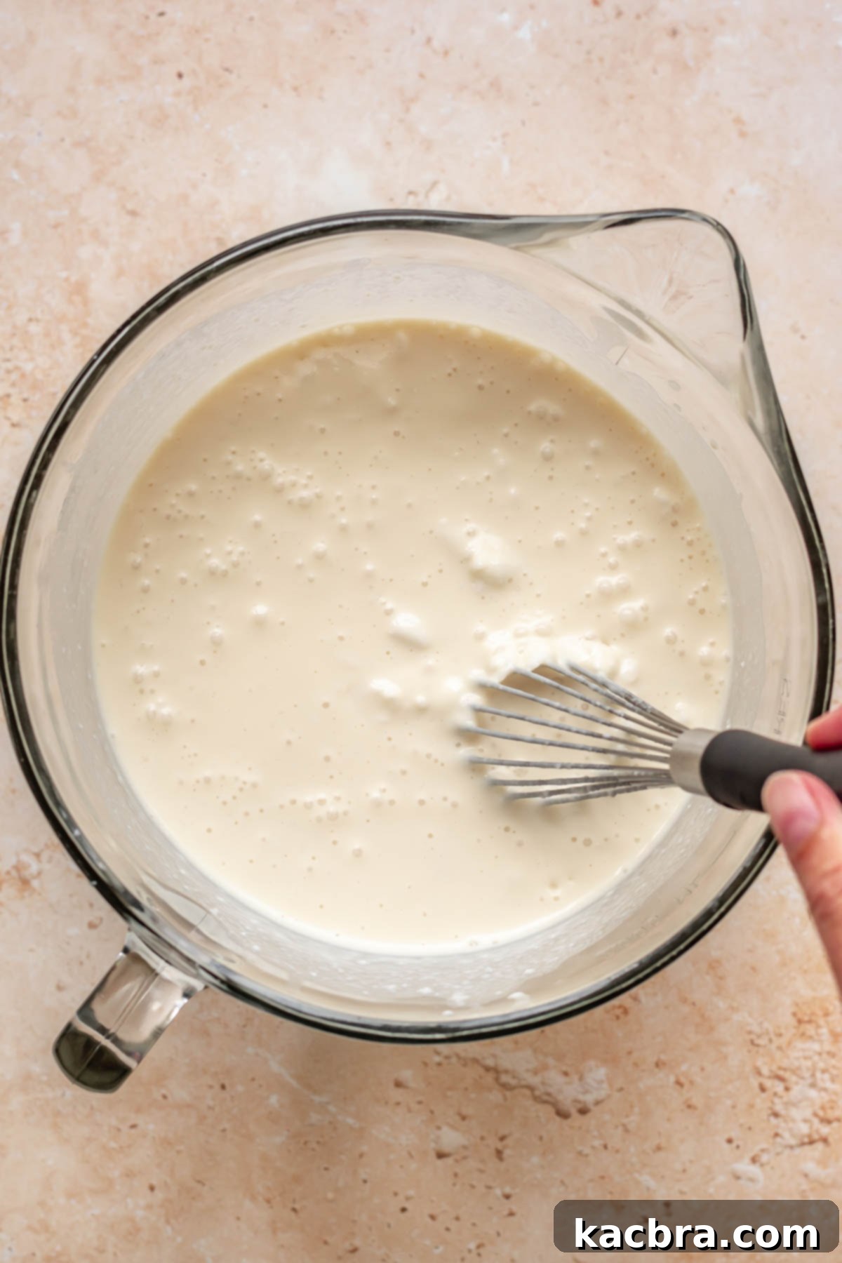 A hand whisks together a mixture of milks in a large measuring cup.