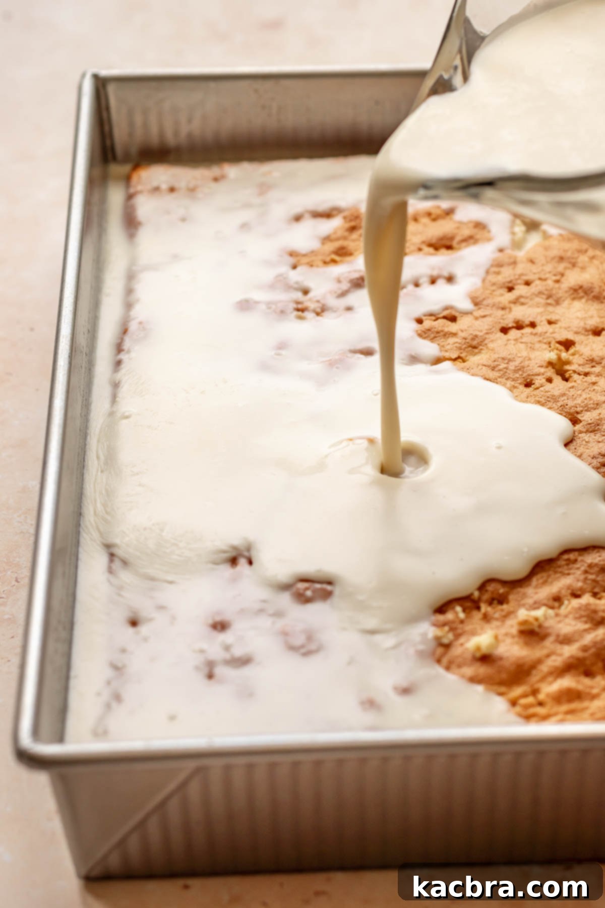 Milk mixture being slowly poured over the poked baked cake.