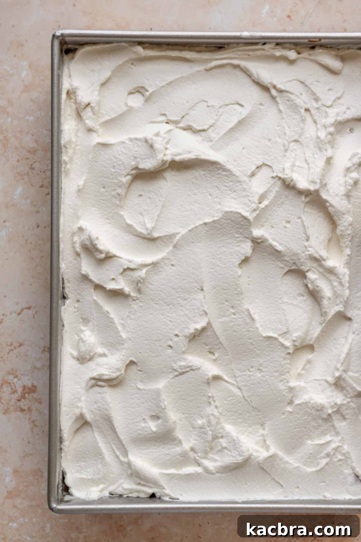 Whipped cream being spread smoothly over the soaked tres leches cake.