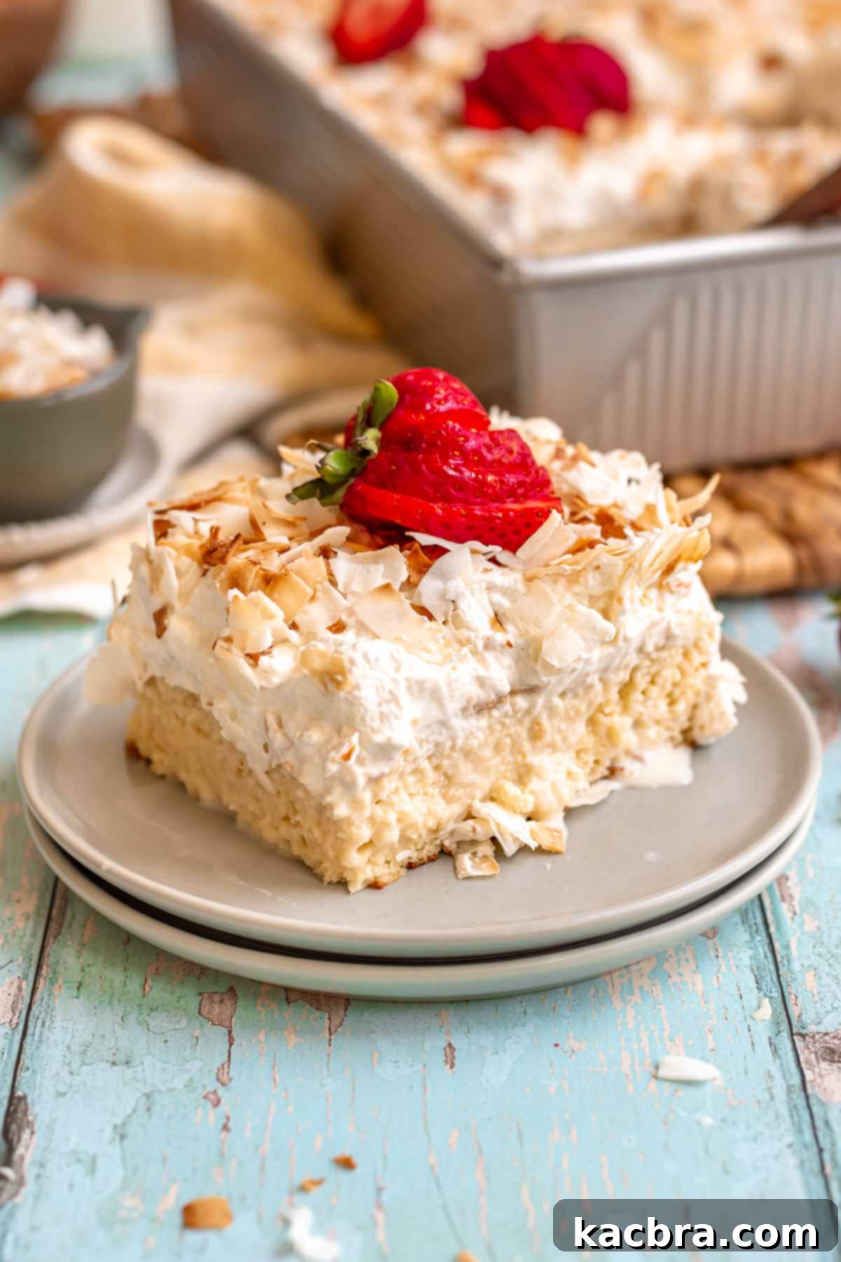 A delectable slice of coconut tres leches cake on a plate, garnished with fresh strawberries.