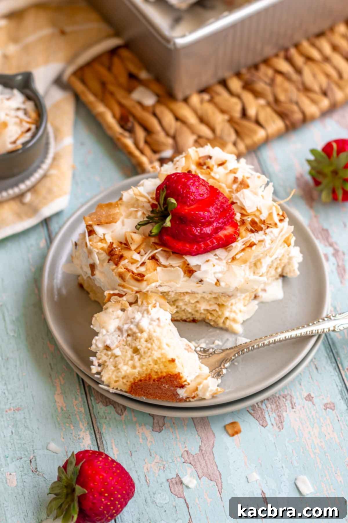 A slice of coconut tres leches cake on a plate, with a fork removing a corner piece.