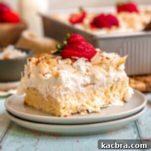 A slice of coconut tres leches cake on a plate with sliced strawberries on top.