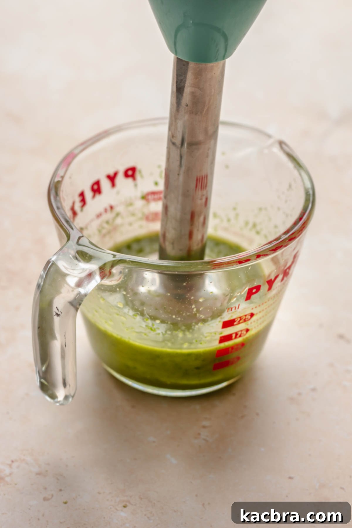 Fresh Burrata Caprese Drizzled with Aromatic Garlic Basil Oil 5 An immersion blender blends basil and garlic oil in a glass measuring cup.