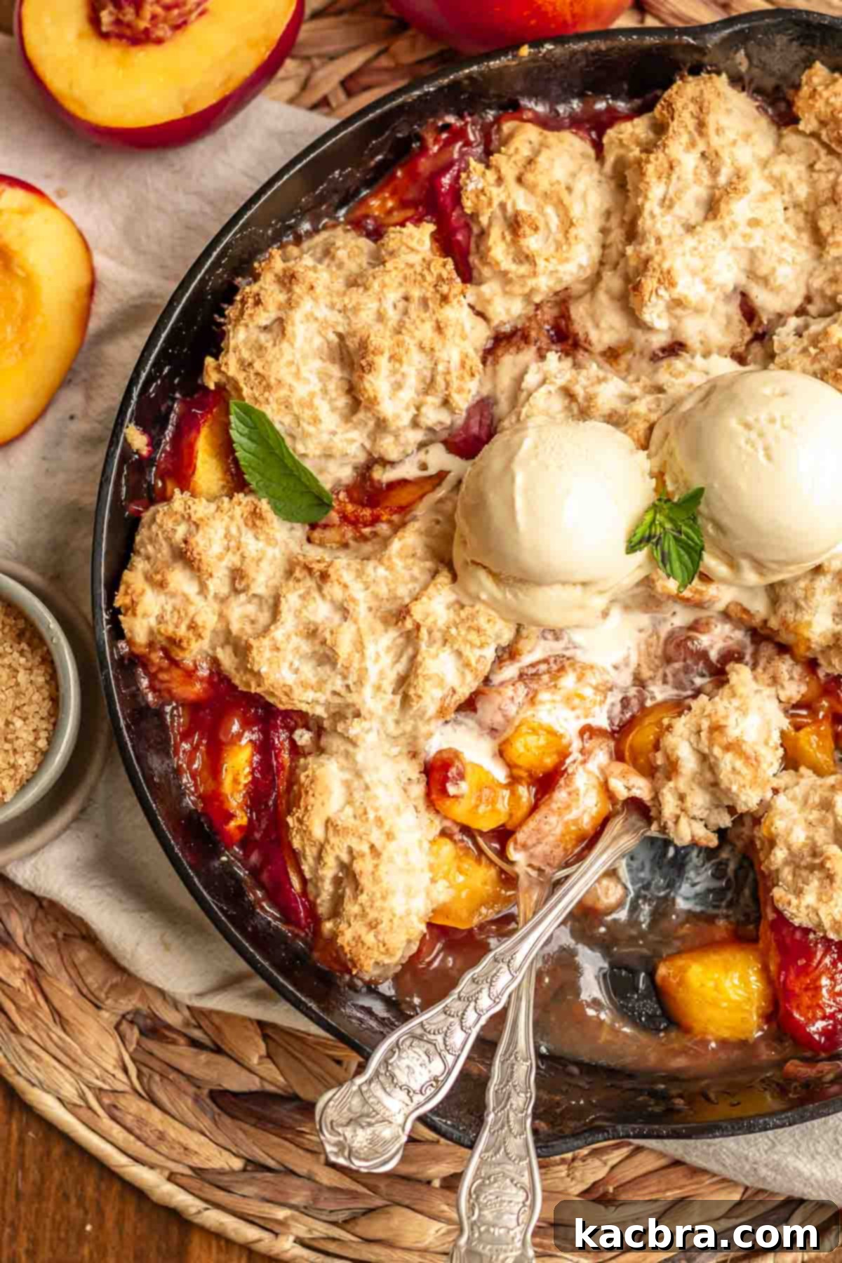 Golden Skillet Peach Cobbler 2 Spoons sitting in peach cobbler. Ice cream sits on top in the middle.