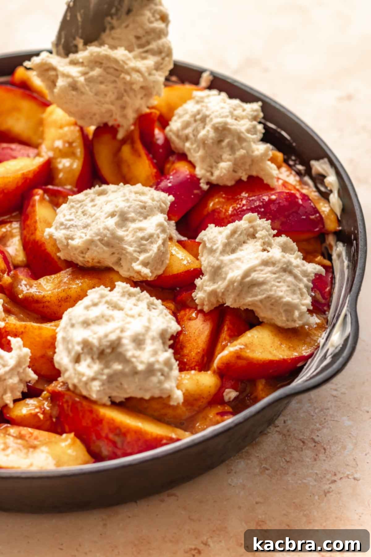Golden Skillet Peach Cobbler 10 A spoon adds dollops of biscuit dough on top of sliced peaches.