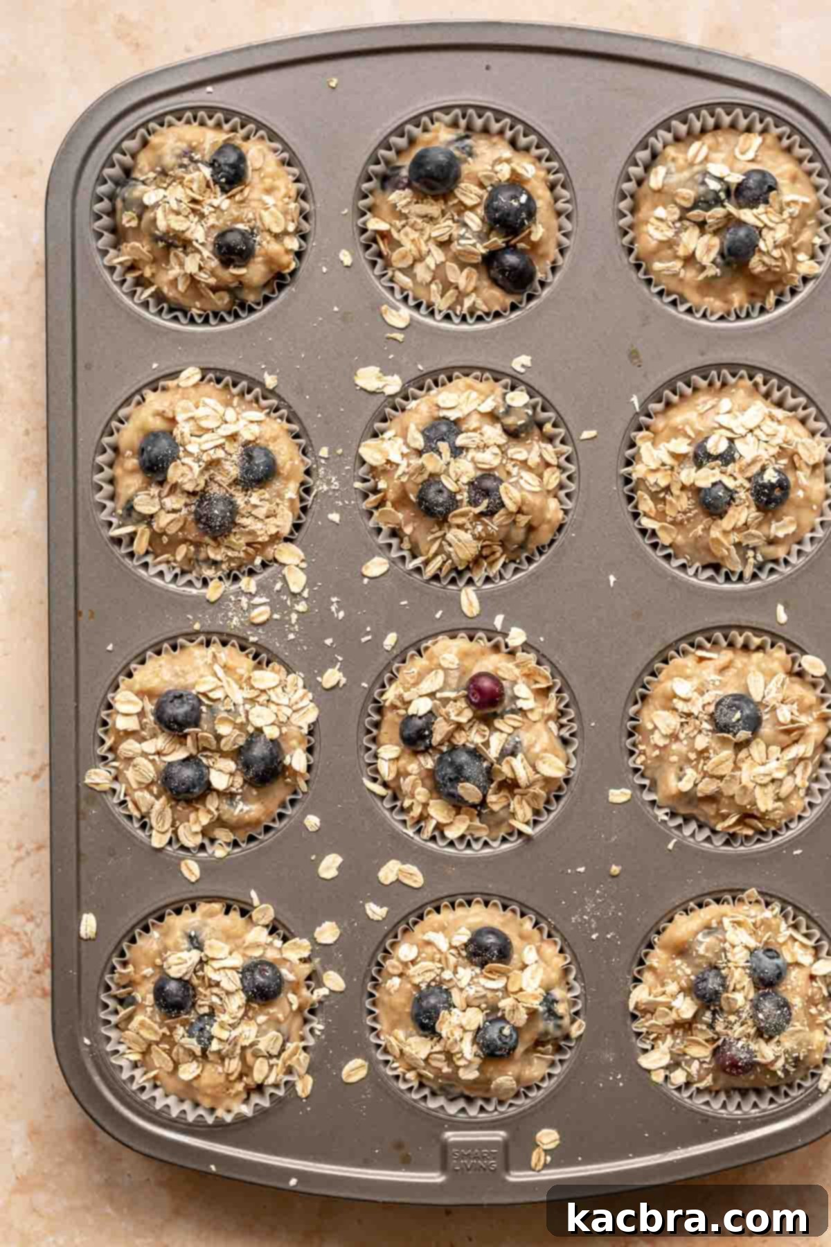 Sweet and Healthy Banana Blueberry Oatmeal Muffins 13 Unbaked muffins in a pan with oats sprinkled on top.