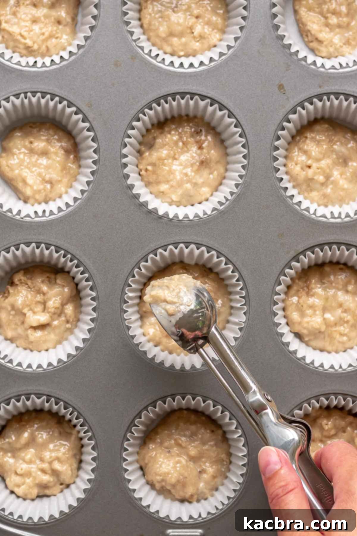 Sweet and Healthy Banana Blueberry Oatmeal Muffins 10 A cookie scoop adding a small amount of muffin batter to cupcake liners in a muffin pan.