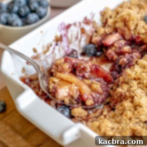 A scoop of apple blueberry crisp on a spoon sitting in a casserole dish.