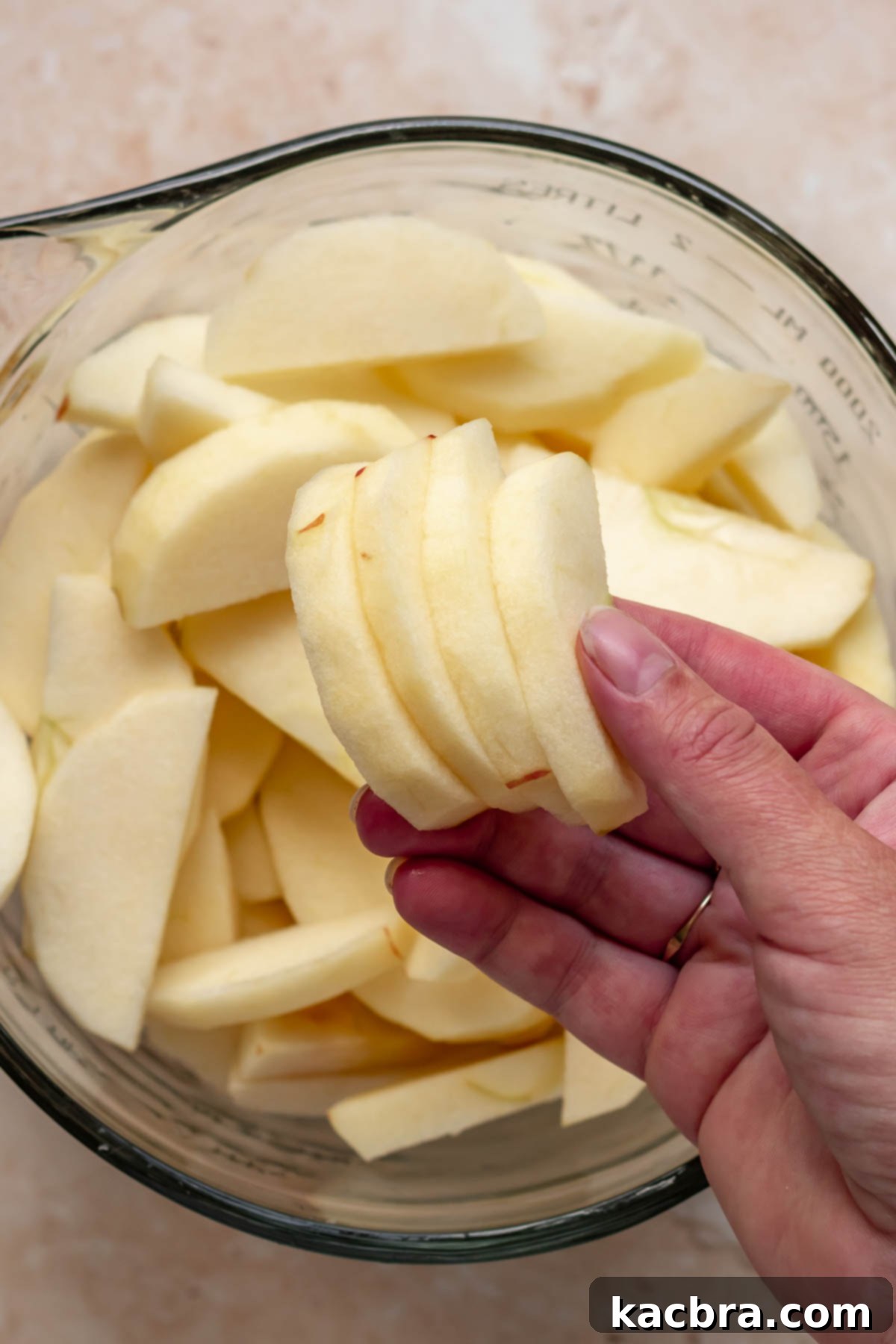 A hand holding sliced apples over a bowl, illustrating the peeling and slicing step.